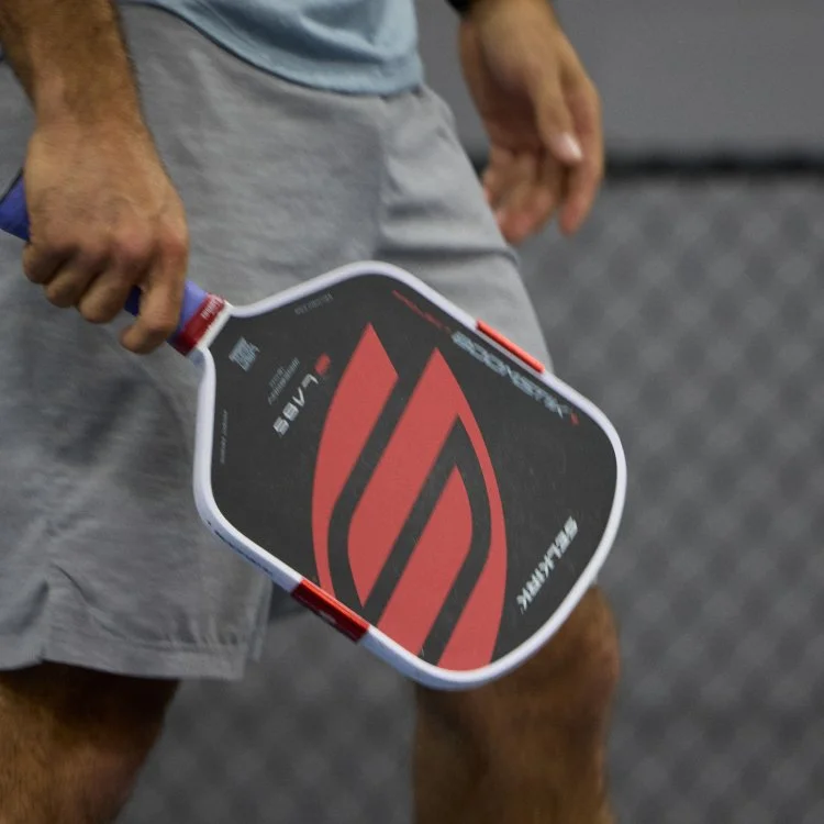 Person holding a paddle tennis racket in a gym or sports facility.