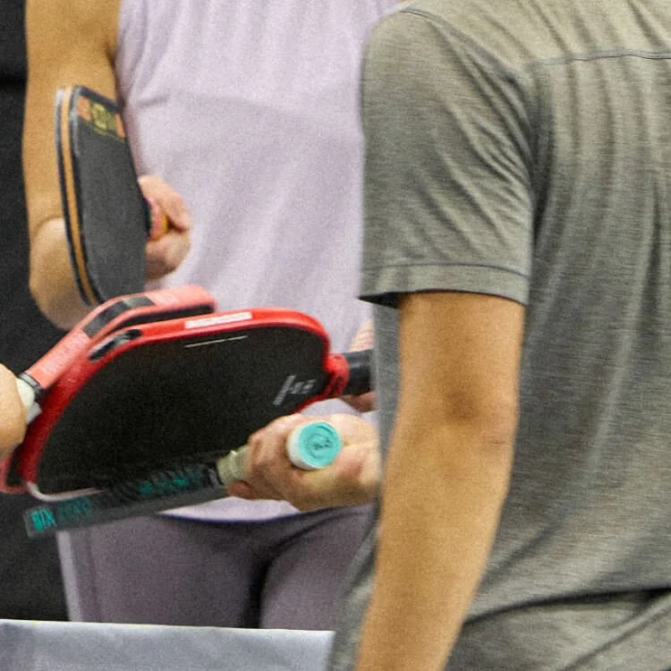 Two people holding pickleball paddles and a ball at an indoor pickleball court.