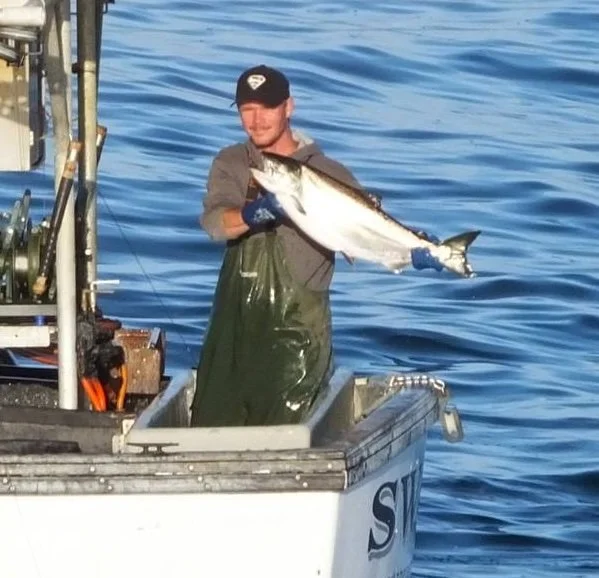 George Bradshaw holding a large salmon on the back deck of. his boat in the water
