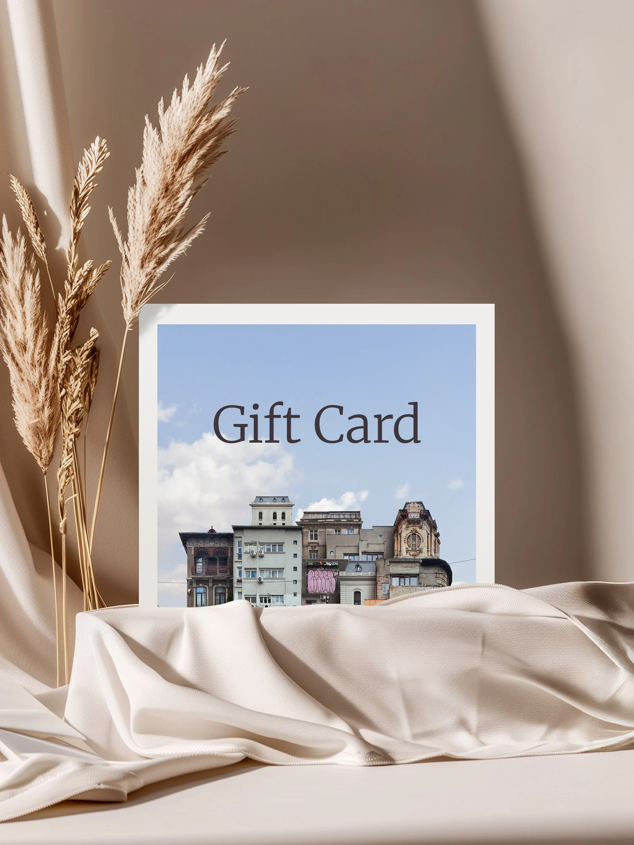Gift card with a cityscape on it, beige fabric, dried pampas grass, and a neutral background.