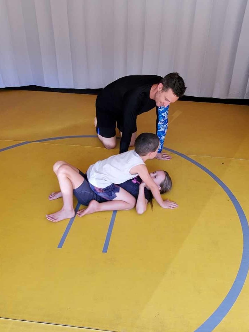 JiuJitsu coach Braxton Hines helping two students practice grappling in Trenton, TX