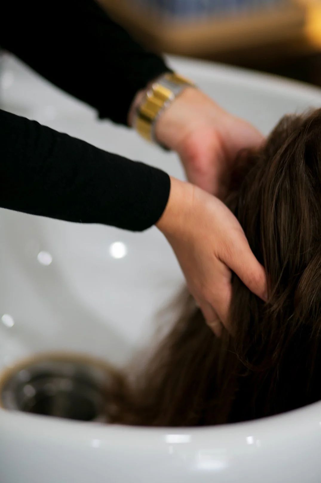 Person's hands washing or rinsing hair in a salon sink.