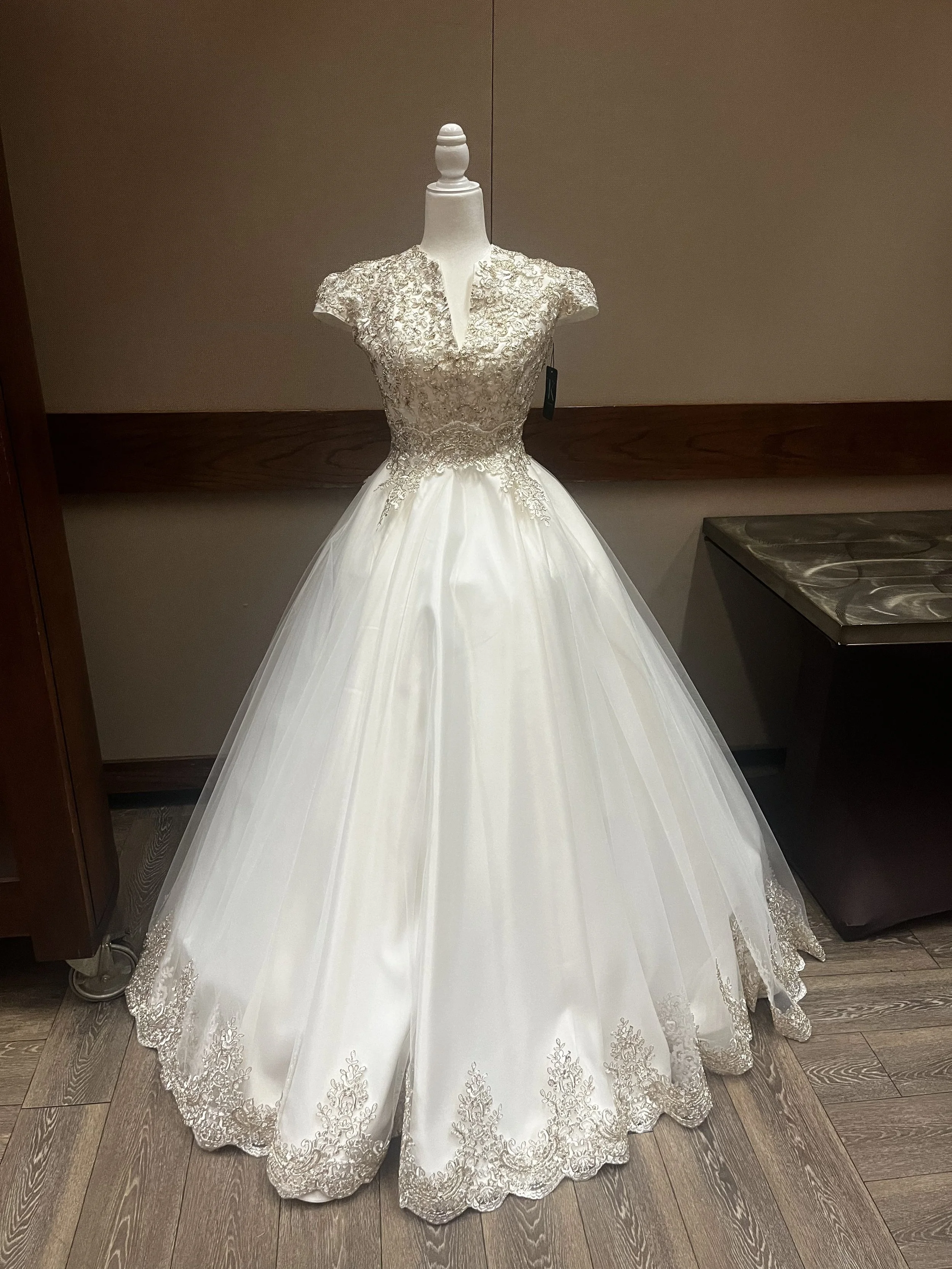 A white wedding dress with a lace embroidered bodice and a full skirt with lace hem, displayed on a mannequin.