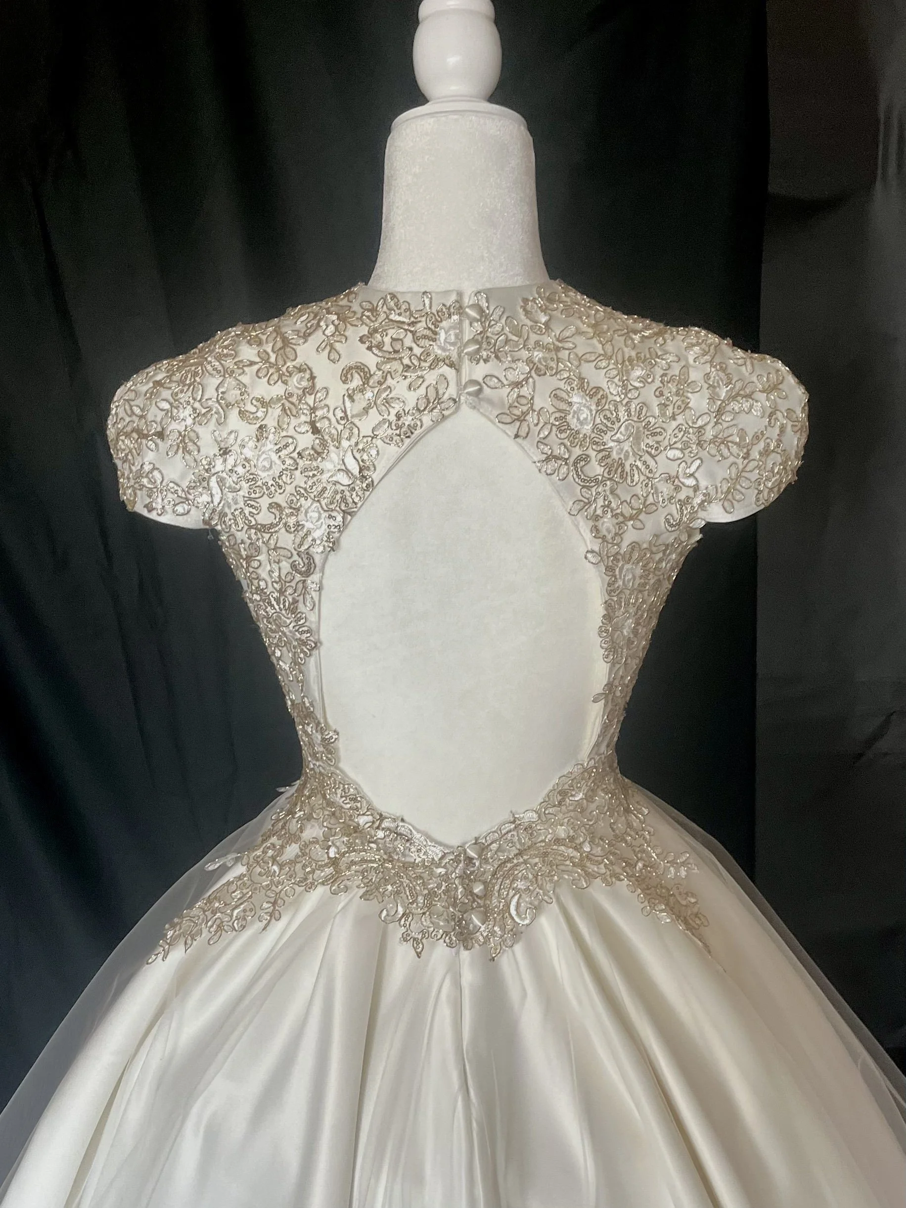 Elegant white wedding dress with intricate gold embroidery on the bodice and shoulders, featuring a large cutout in the front.