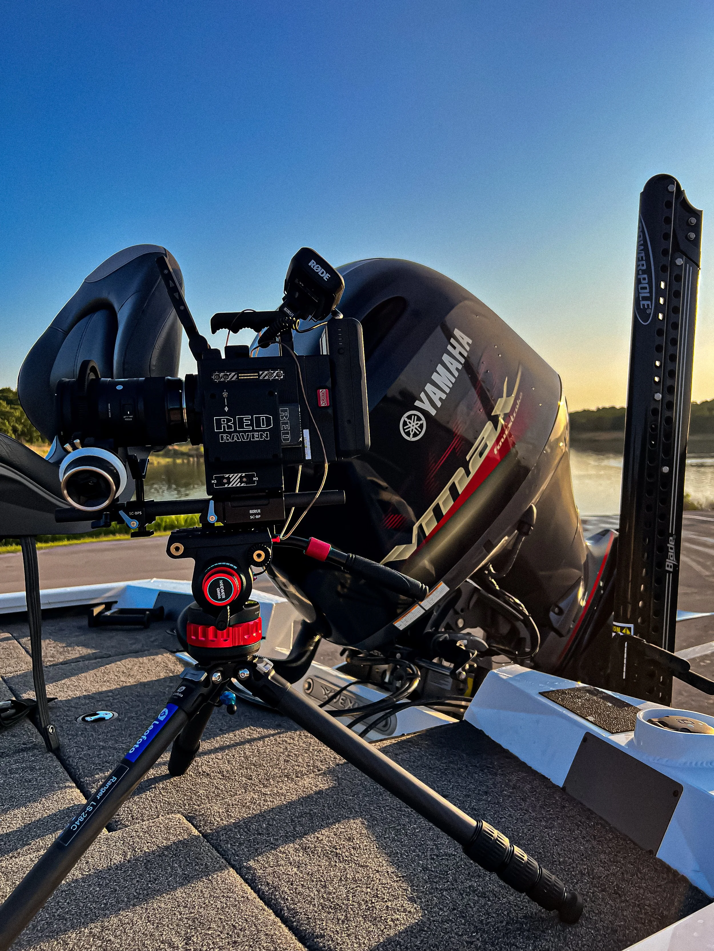 Close-up of a Yamaha outboard motor on a boat with a camera mounted on a tripod in the foreground, during sunset near a body of water.
