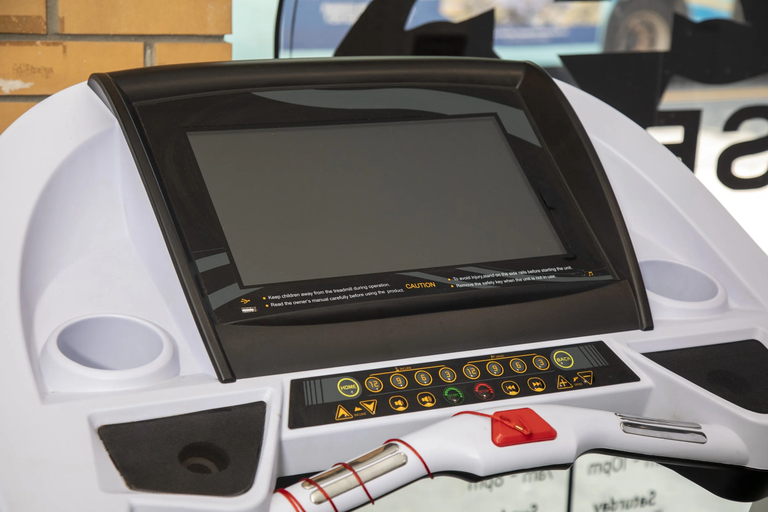 Close-up of a white treadmill with a digital control panel, black and yellow buttons, and caution labels, with electrical wiring and pens nearby.