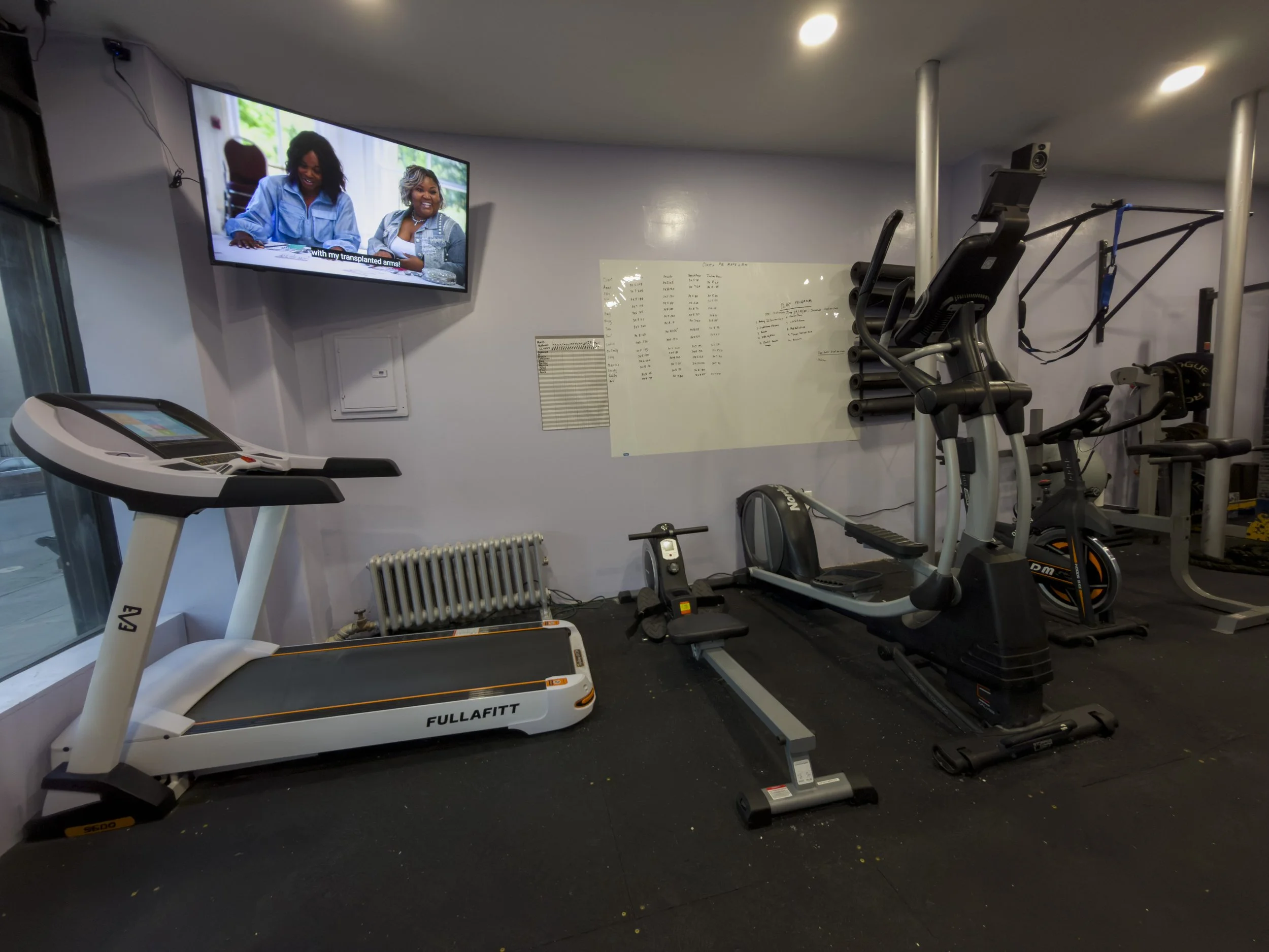 Home gym with treadmill, rowing machine, stationary bike, TV, whiteboard, and workout equipment.