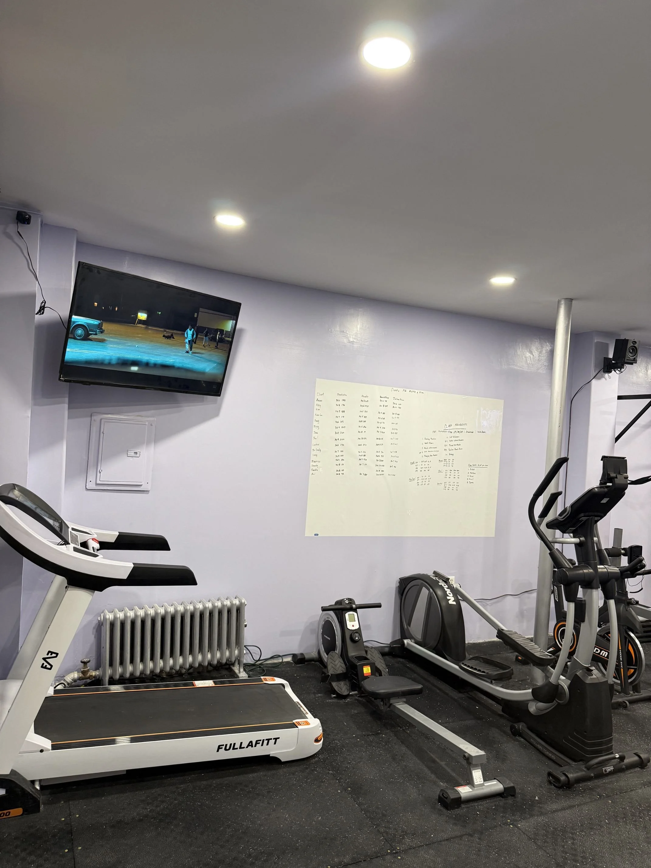Gym with treadmill, rowing machine, elliptical trainer, and a wall-mounted TV showing an outdoor scene.