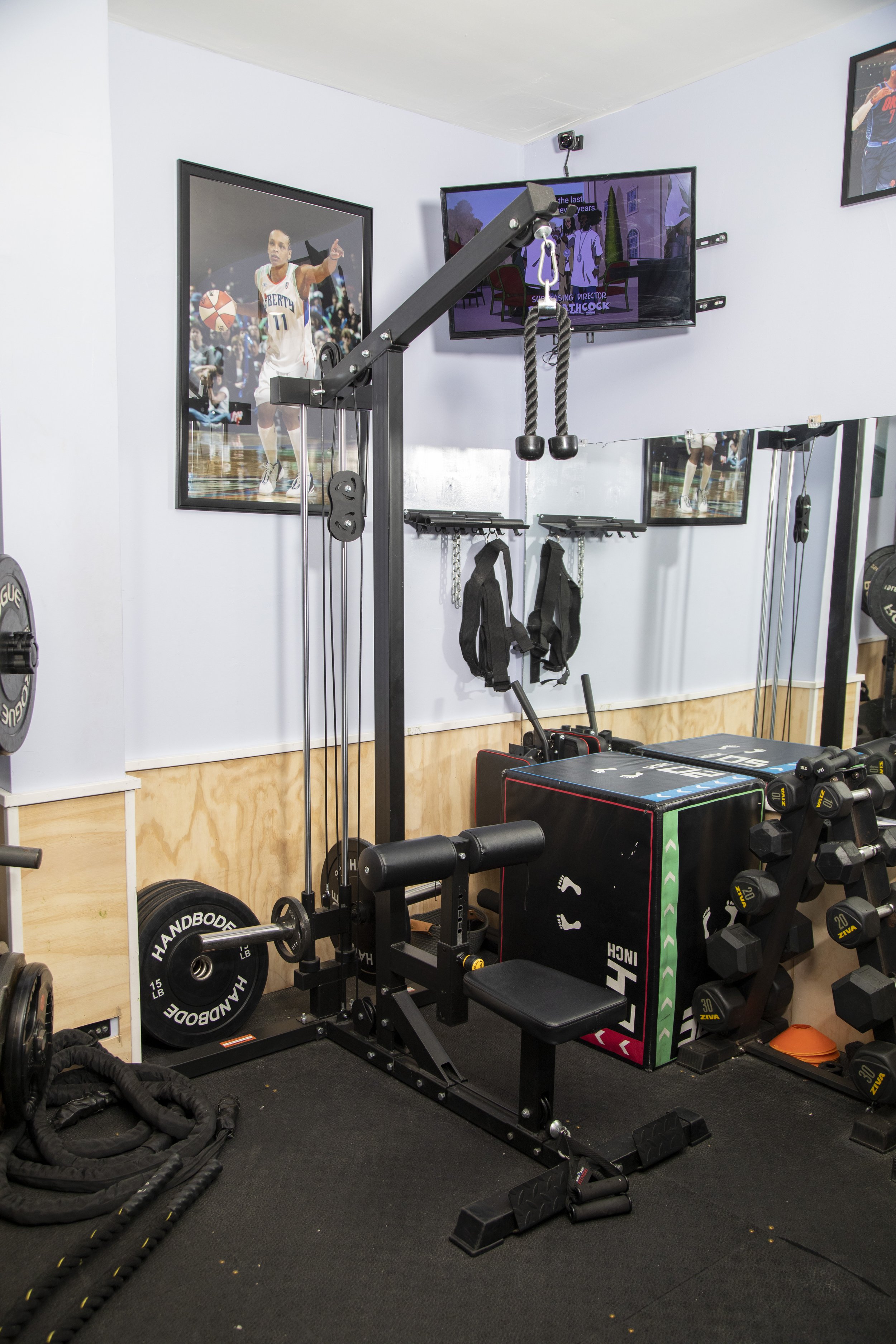 A home gym with fitness equipment including a rowing machine, weights, resistance bands, a plyometric box, and motivational posters on the wall.