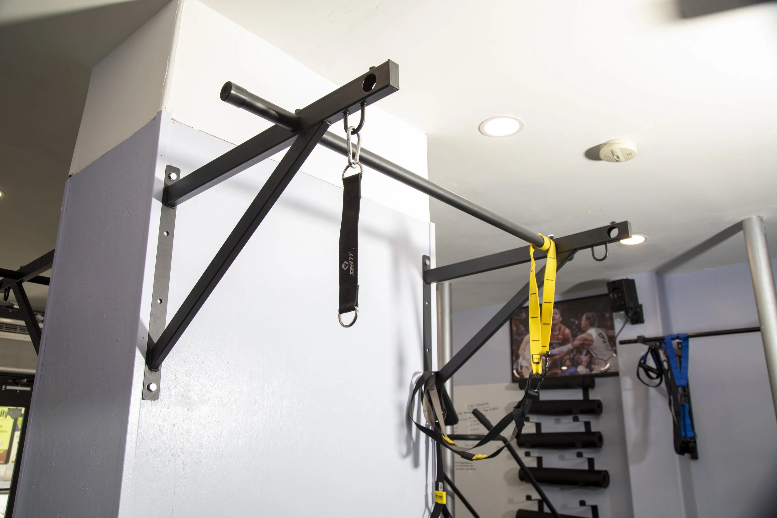 Pull-up bar and suspension training straps mounted on a wall in a fitness gym.