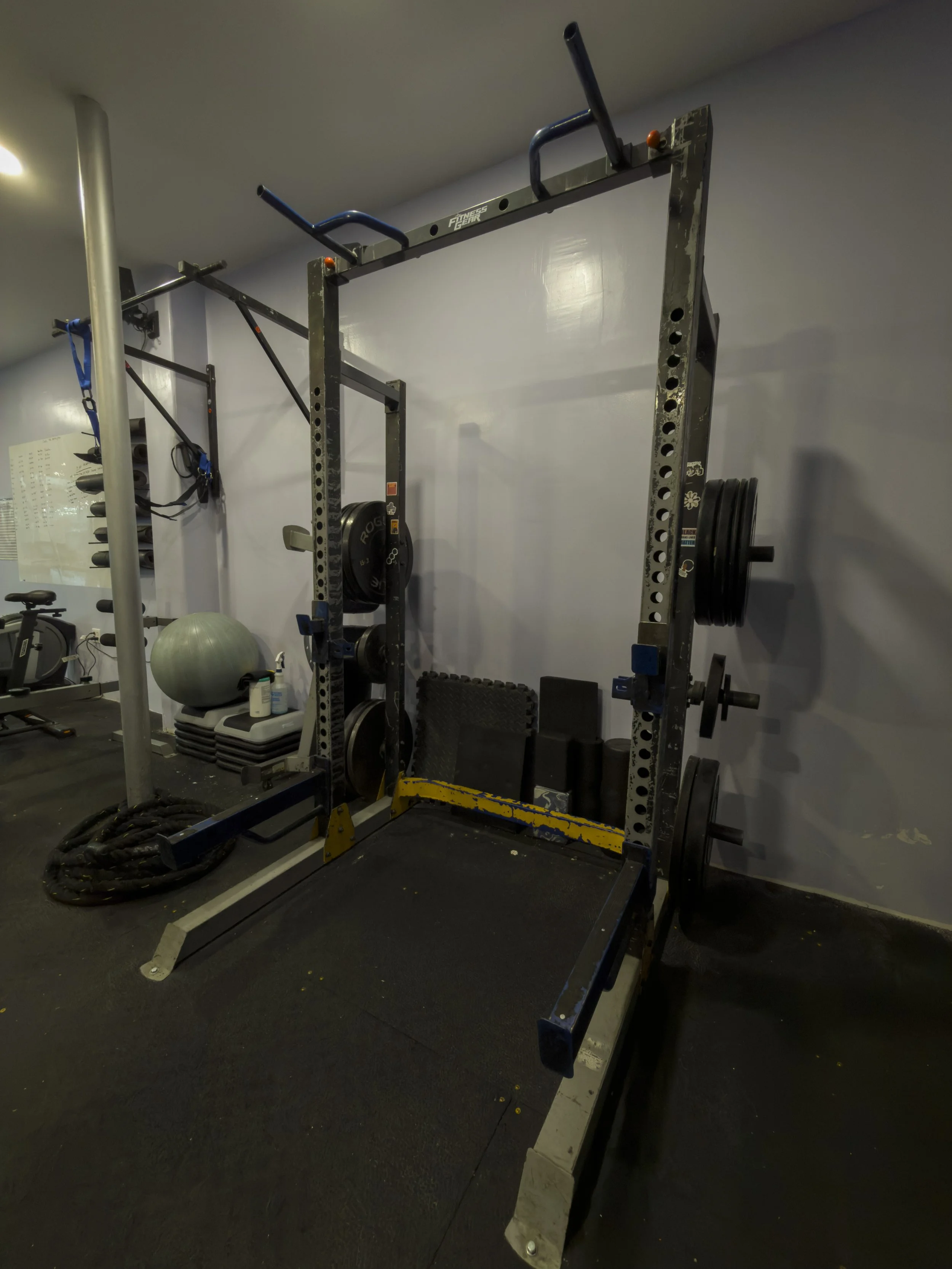 Empty squat rack with weights, a black mat, and nearby exercise equipment in a gym.