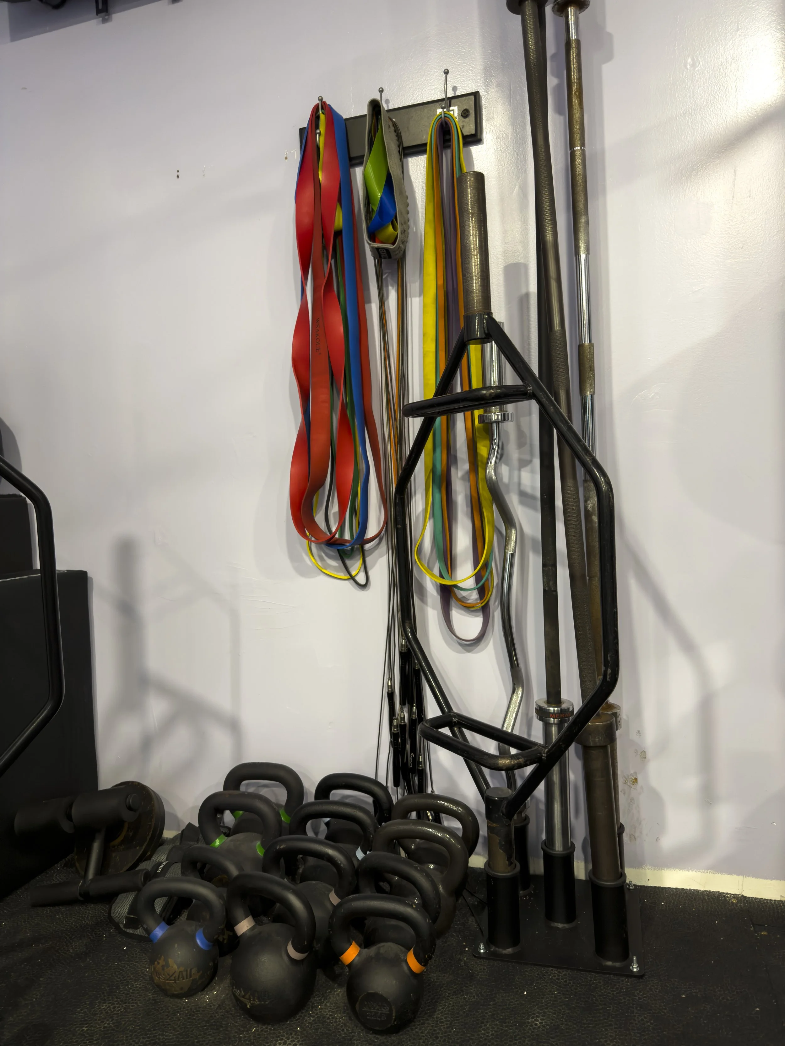 Workout area with resistance bands hanging on a wall, resistance training bars, and kettlebells on the floor.