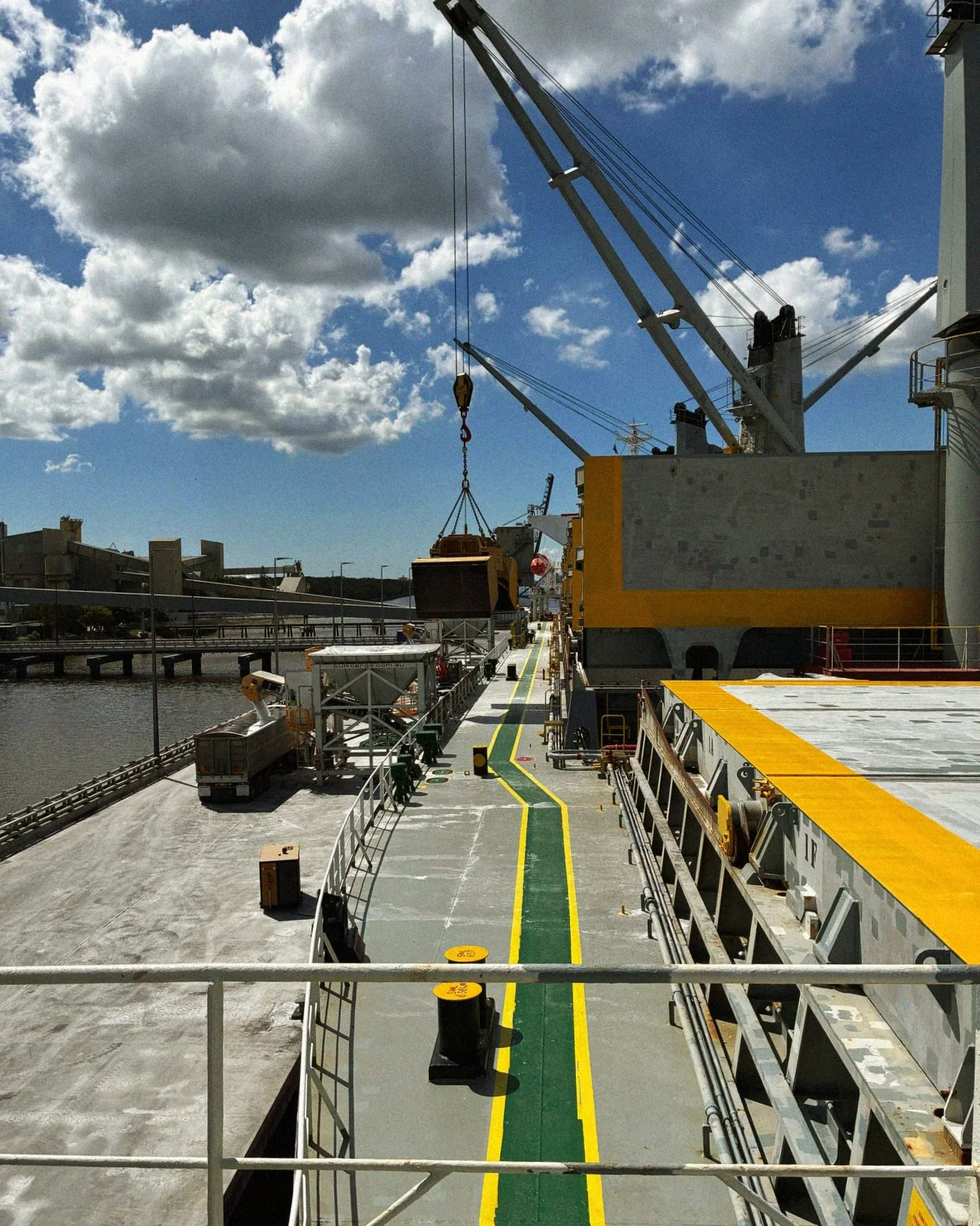 View of a docked ship's deck with a crane lifting a cargo container under a partly cloudy sky.