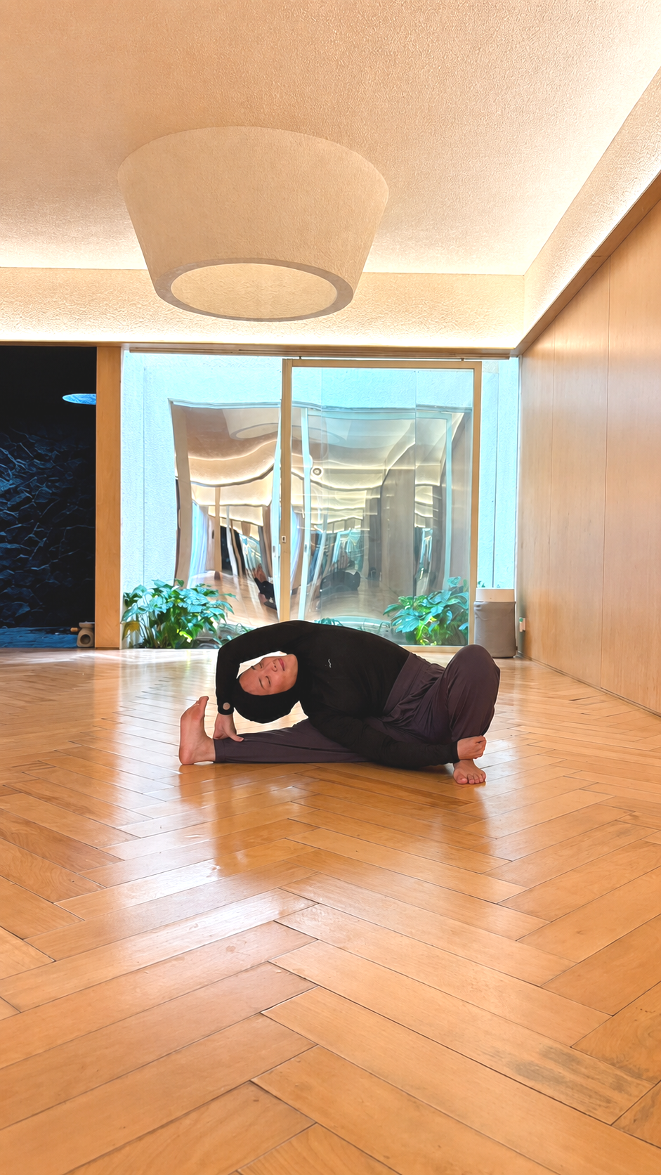 Person in a hijab performing a side bend yoga pose on a pink mat indoors.
