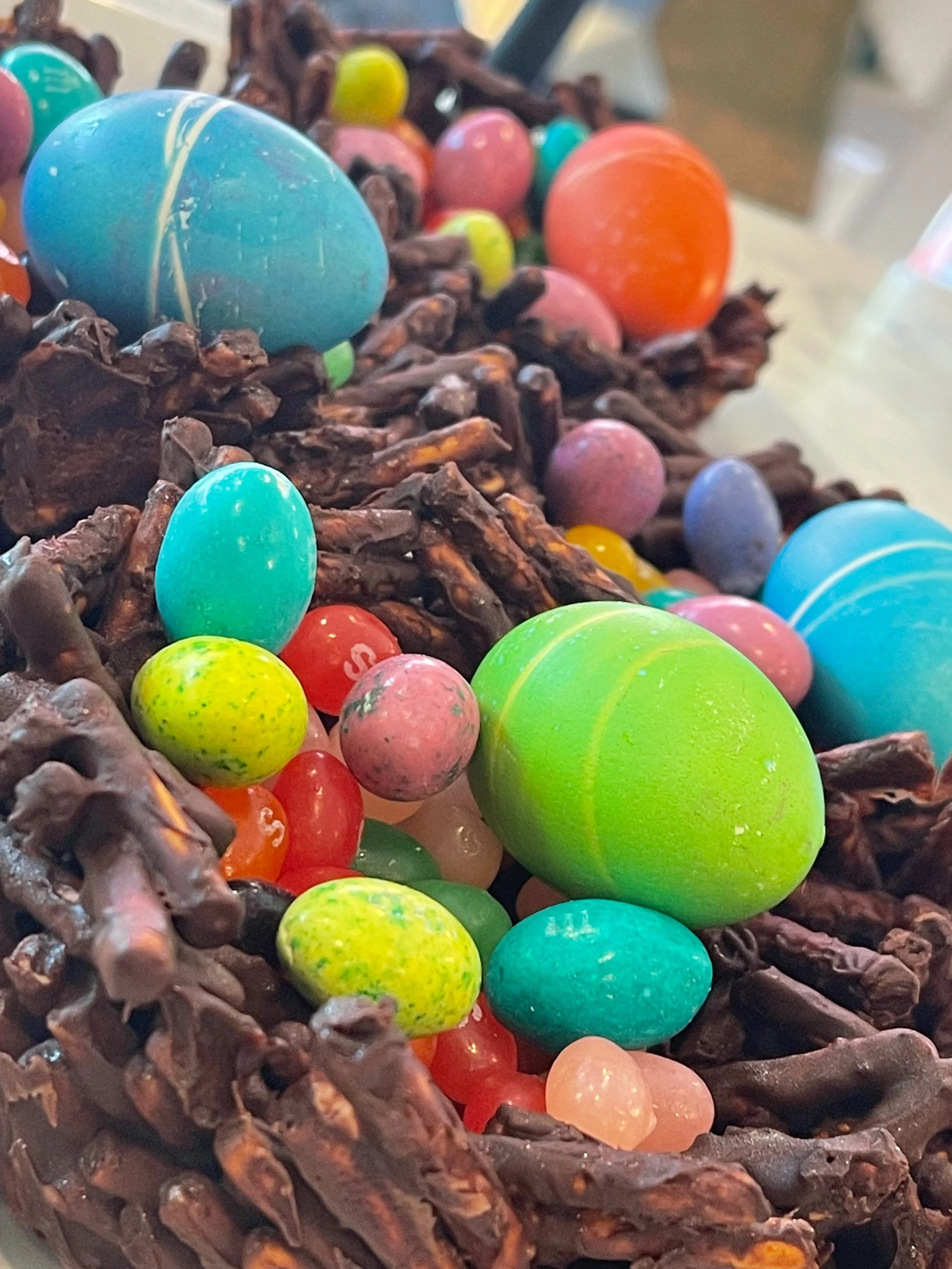 Close-up of chocolate nest filled with colorful plastic Easter eggs.