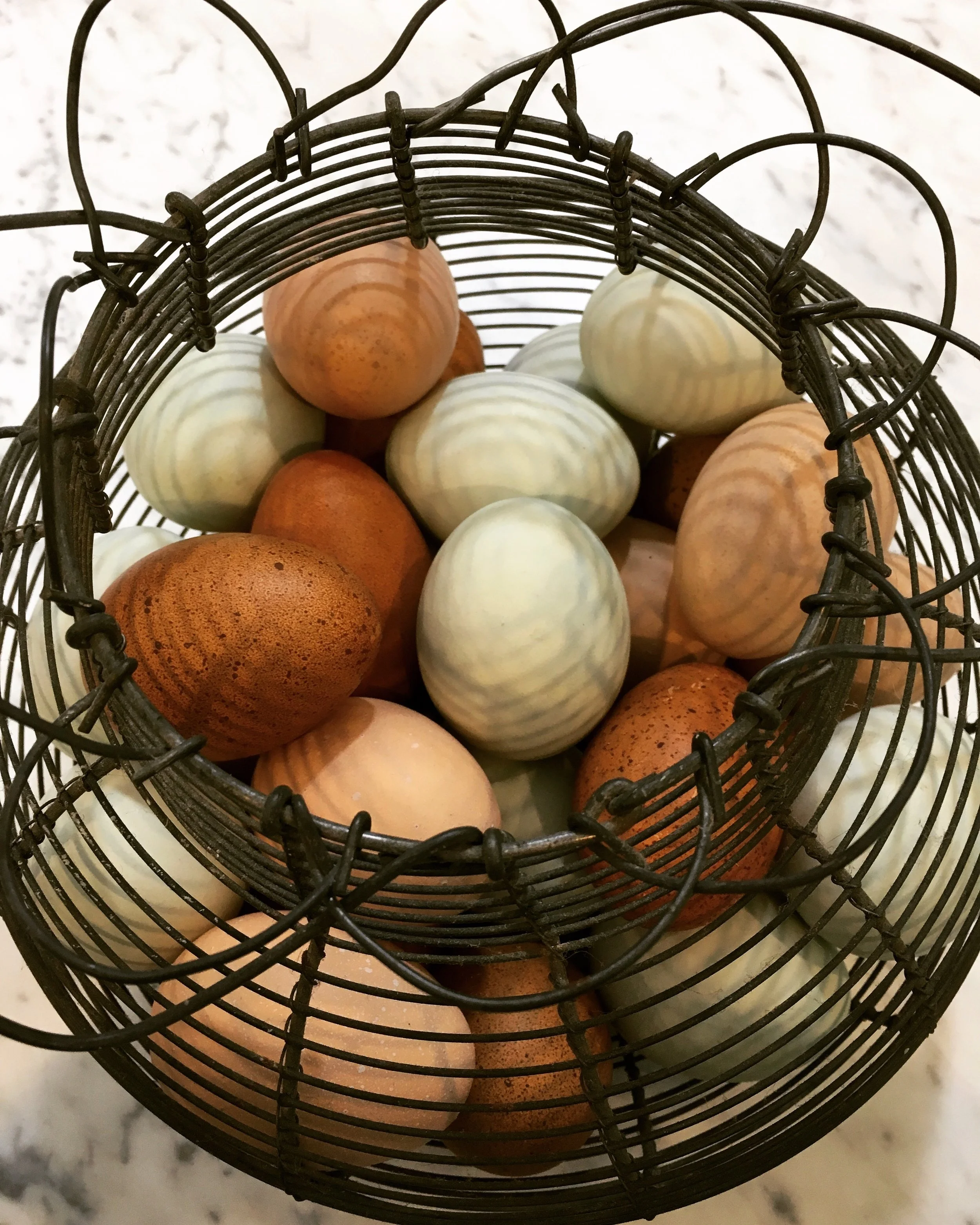 A wire basket containing several pale and brown eggs resting on a light marble surface.
