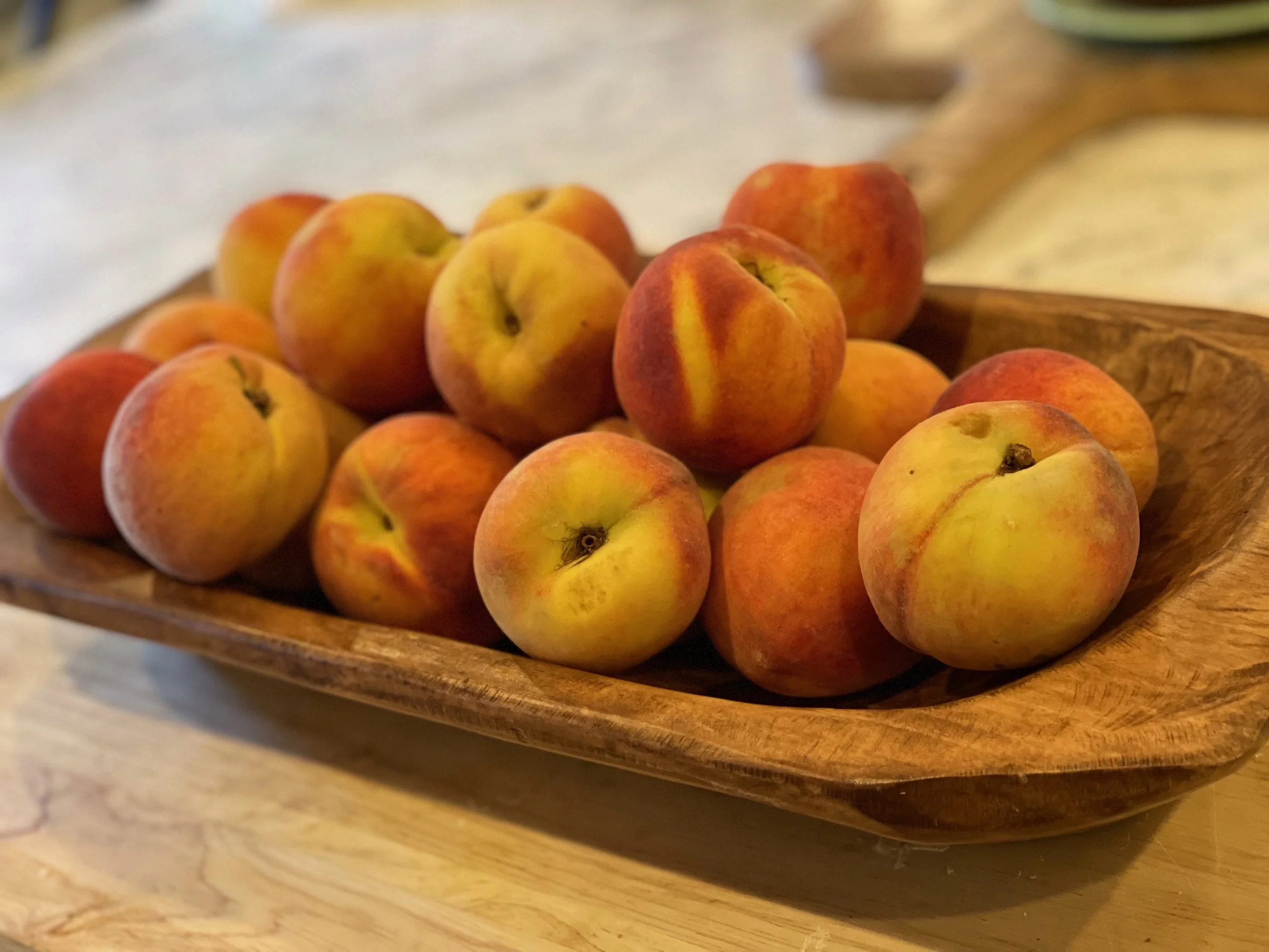 A wooden bowl filled with fresh peaches resting on a wooden surface.