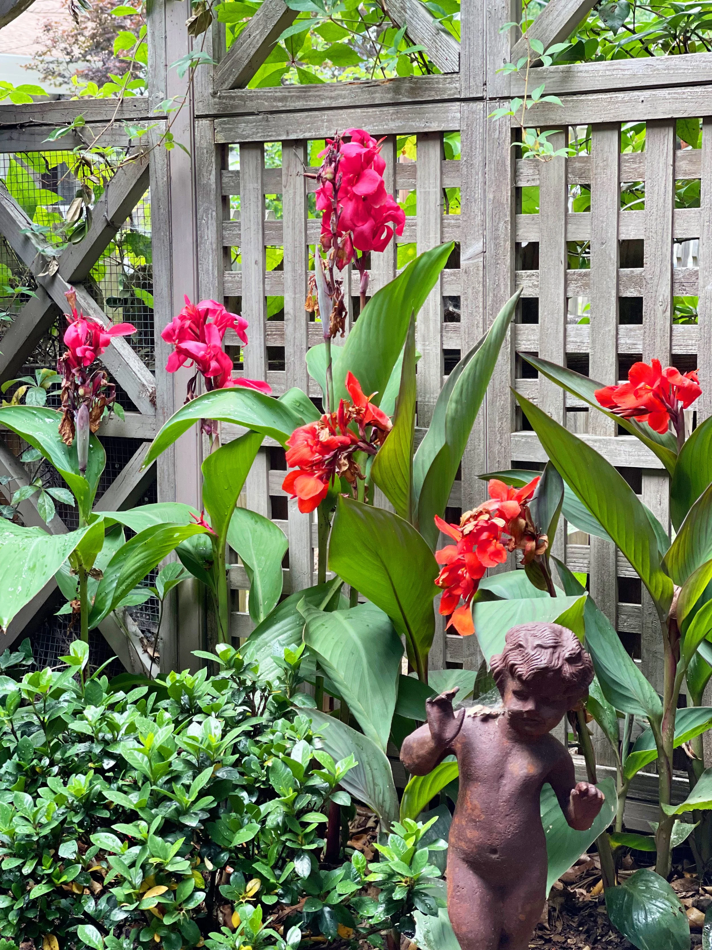 Colorful flowers and a small decorative statue in a garden with a wooden lattice background.