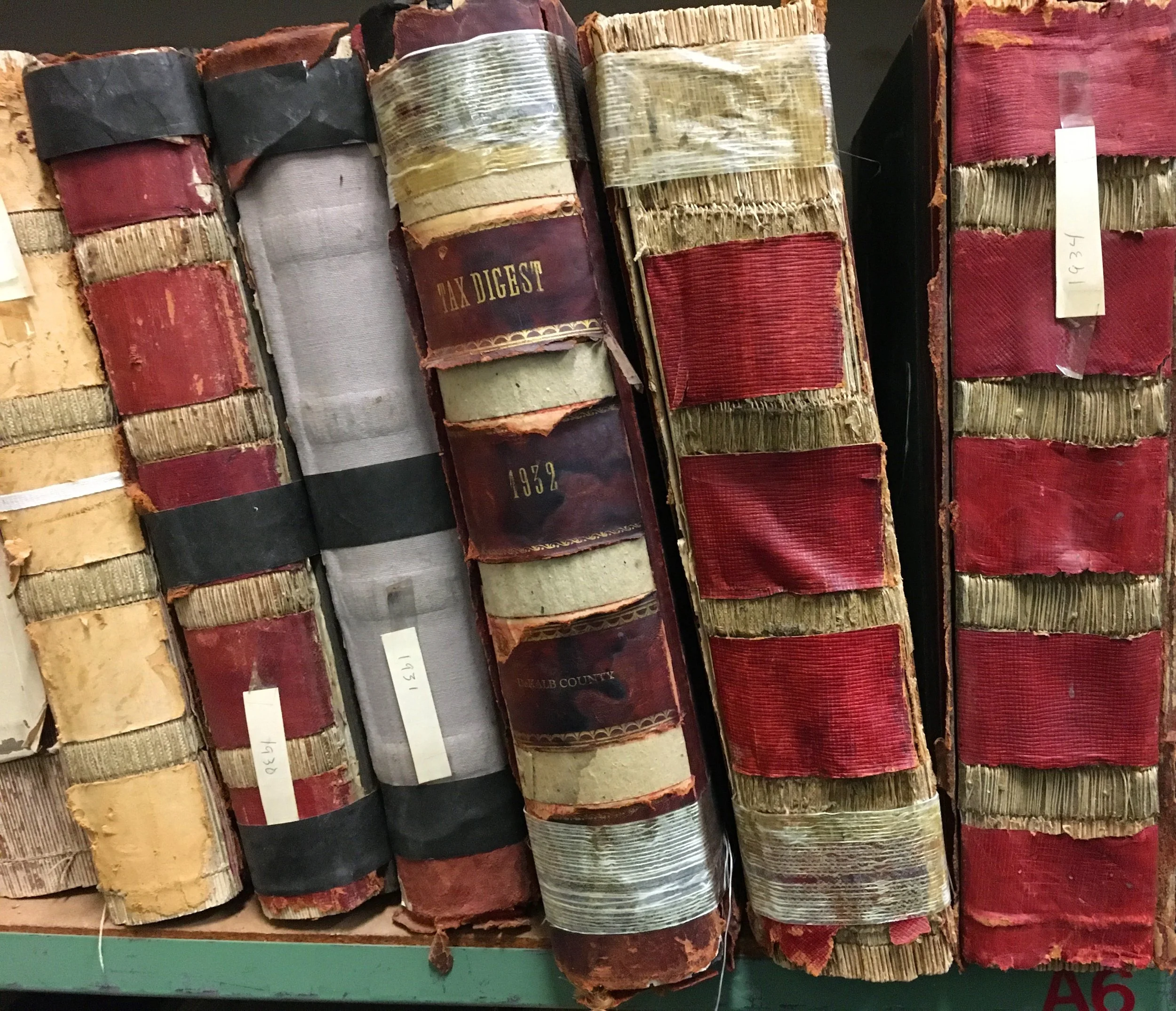 Old, worn books with faded covers, stacked on a shelf. Some labels and titles visible, including 'Max Digest' and year 1932.