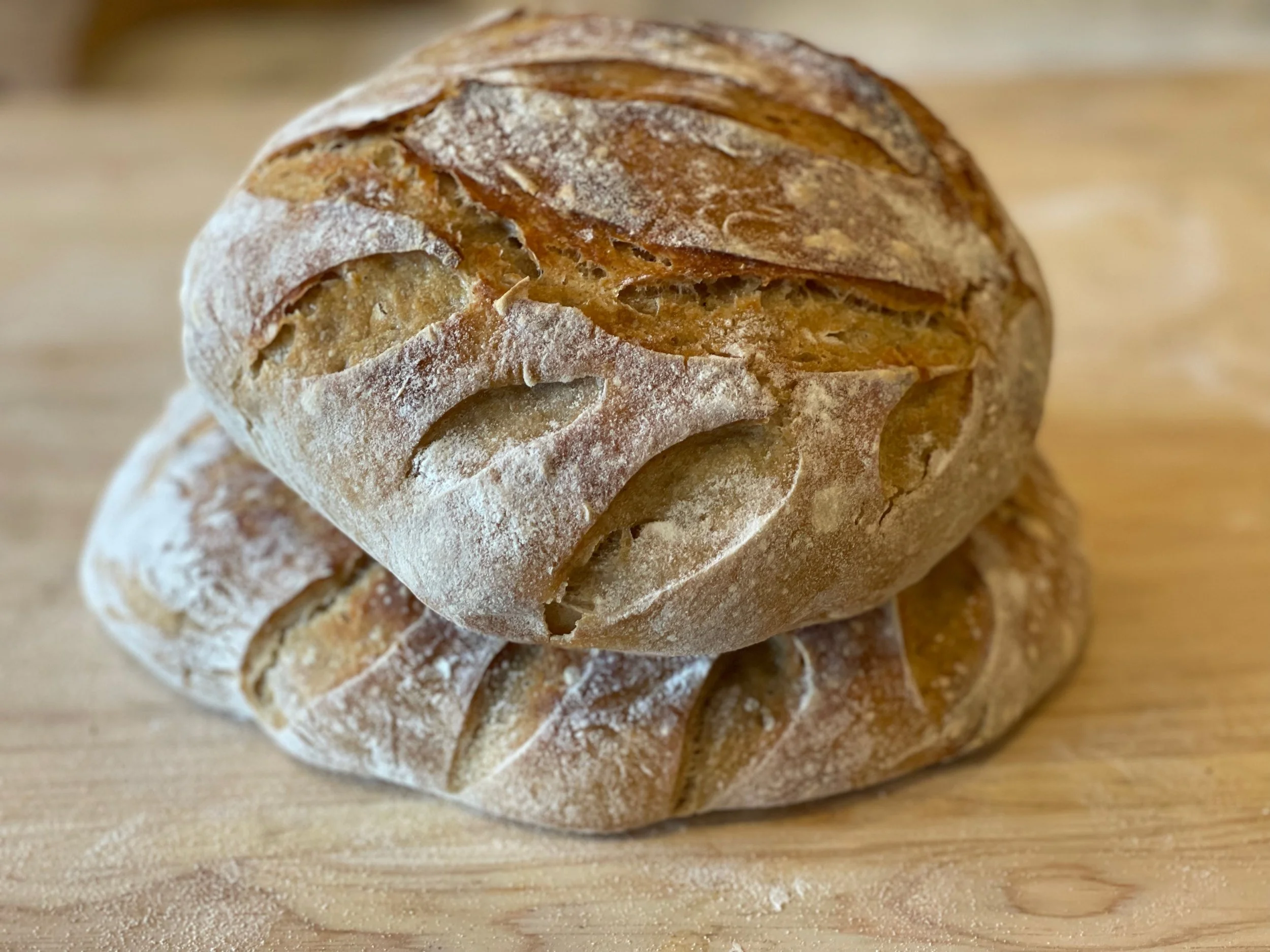 Two loaves of freshly baked crusty bread on a wooden surface.