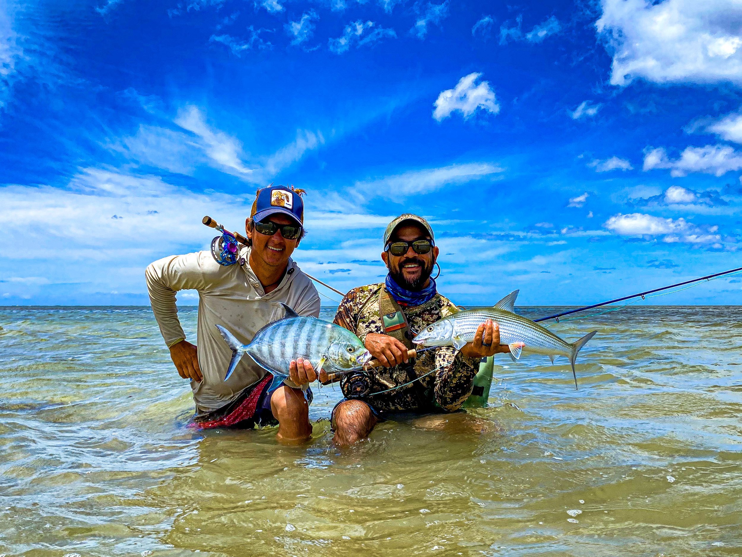 Two anglers kneel in the shallow ocean flats of Molokai, each holding a fish