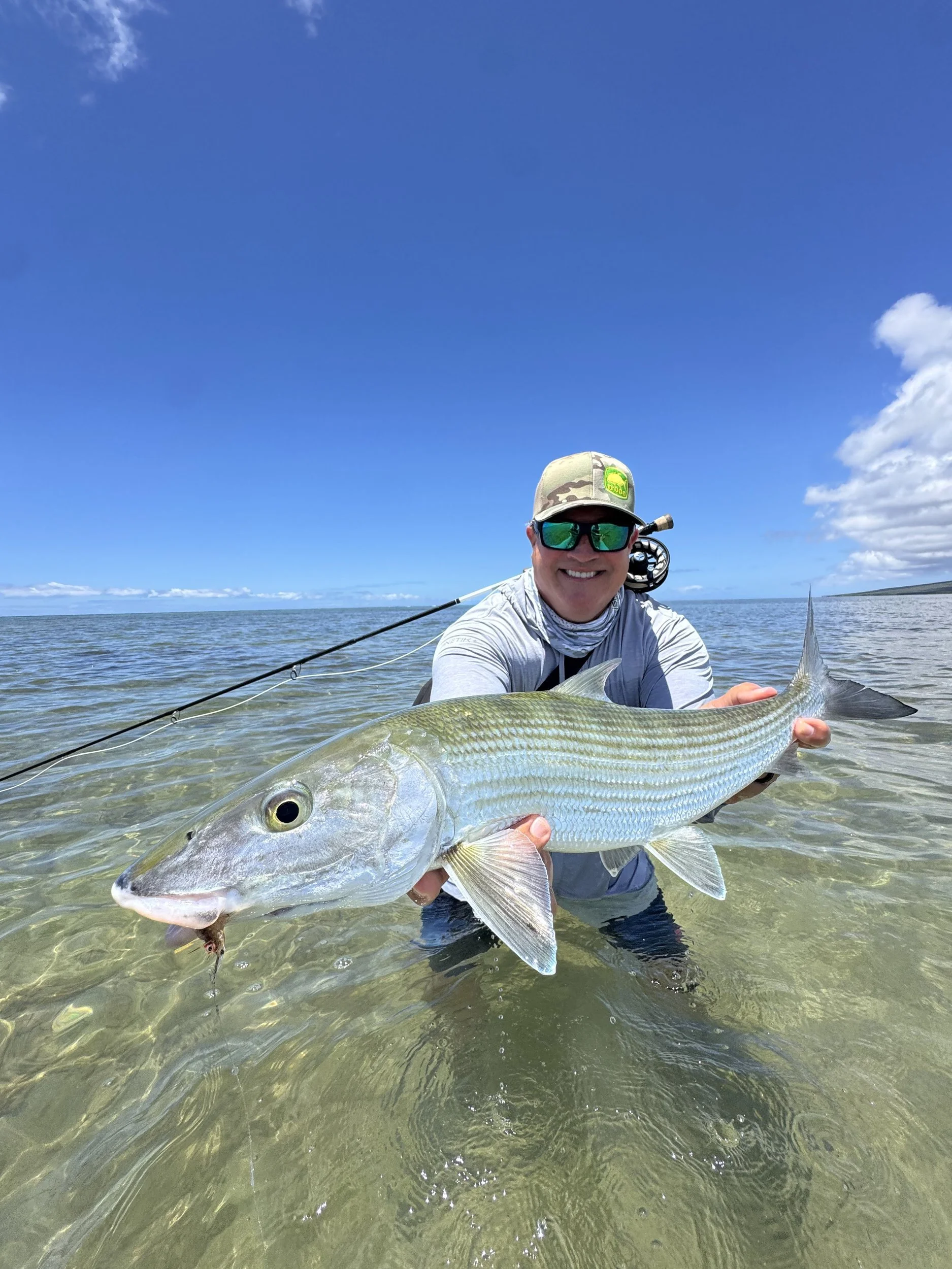 Angler holding a bonefish in clear water under a blue sky off Molokai