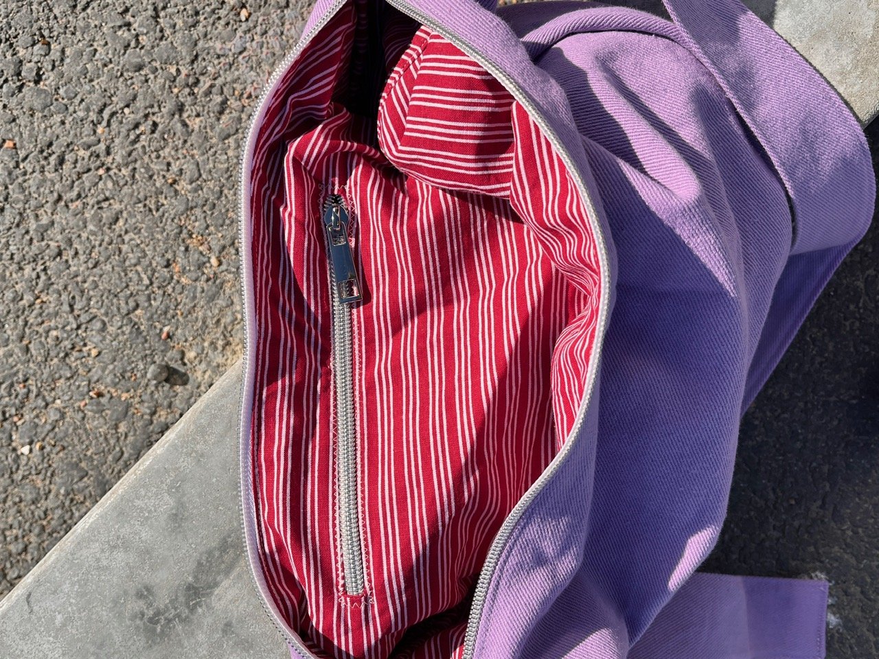 Open orchard collection lupin- purple handmade denim crossbody Longies bag with recycled unique lining red and white striped interior lining and a zipped pocket inside, placed on a concrete surface.