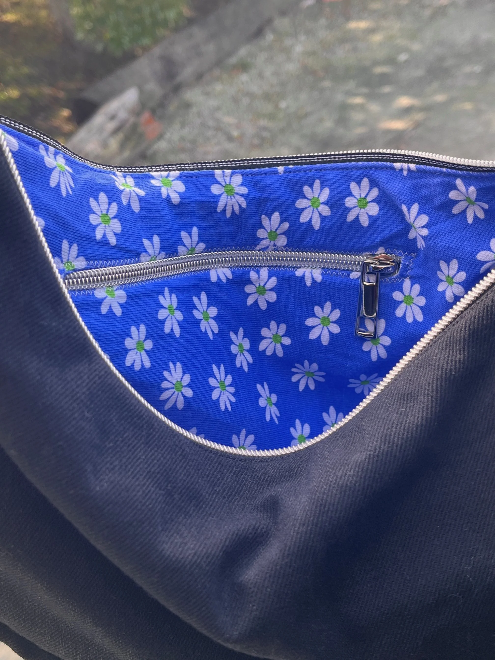 upcycled lining of a handmade denim Longies bag with a blue floral pattern lining featuring white daisies with green centers and a silver zipper.