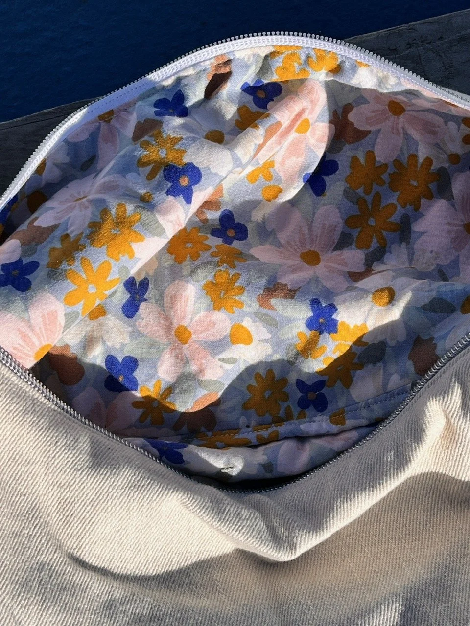 Open zipper bag displaying floral patterned upcycled lining fabric with pink, yellow, blue, and brown flowers. Black denim crossbody bag from Longies.