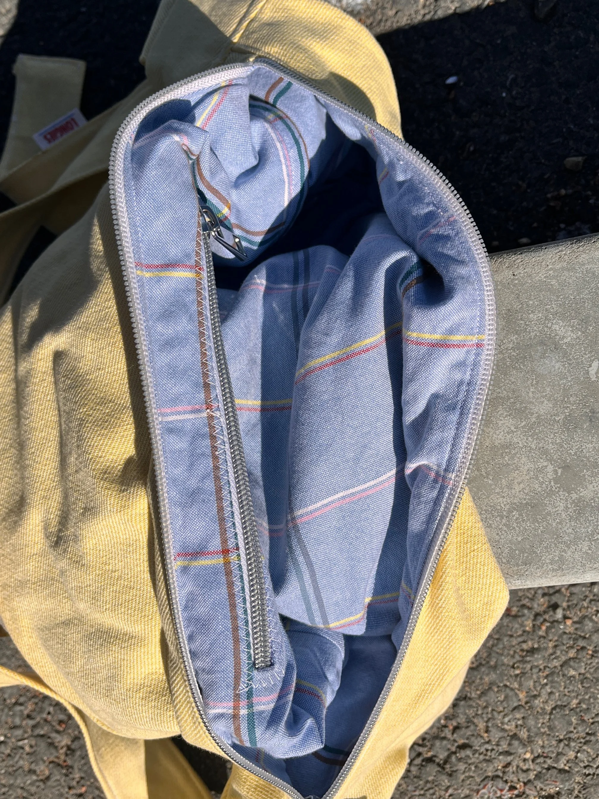Open butter yellow handmade Longies bag with an upcycled unique lining in blue and plaid lining, placed on a concrete surface outdoors.