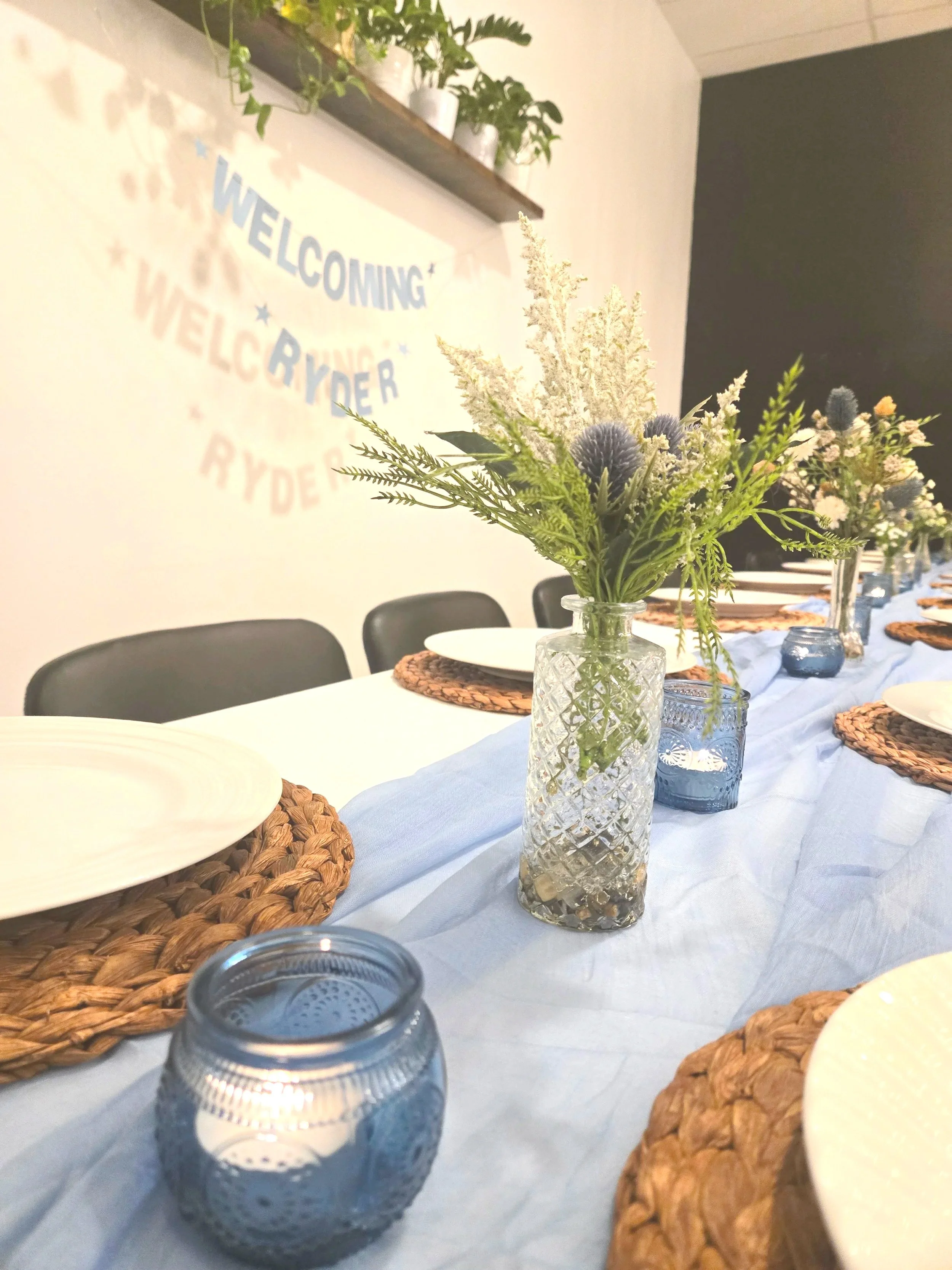 Blue candles and flower budvases with wicker chargers on table at Oasis Collective baby shower in Sarasota, FL