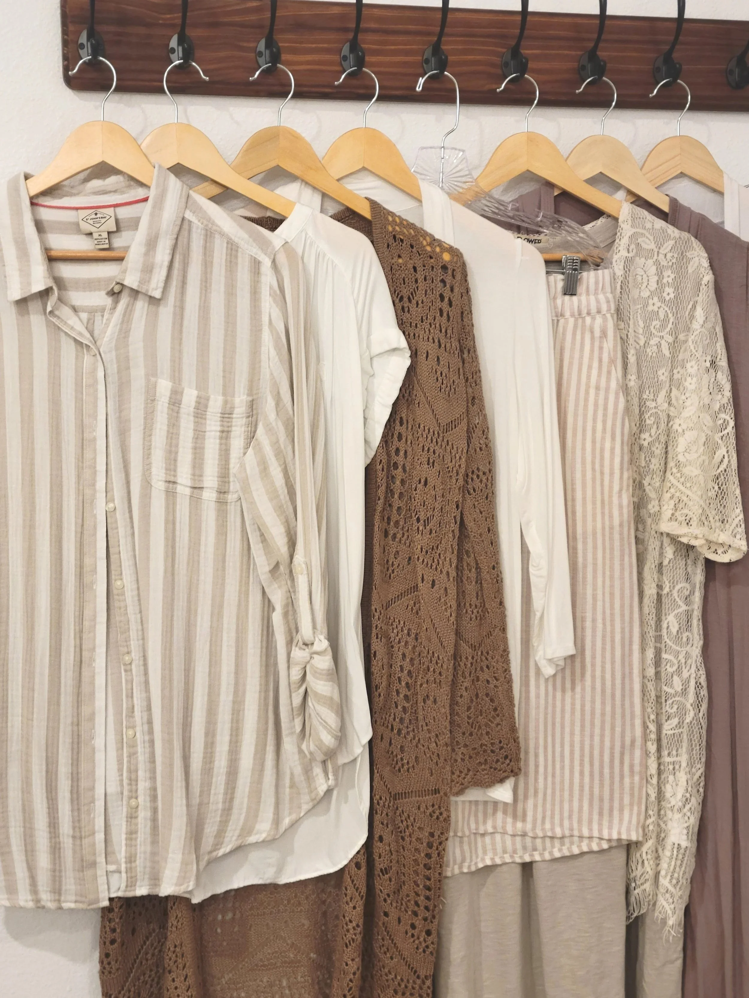 Display of hanging women's clothing including shirts, Blouses, and lace dresses on wooden hangers.