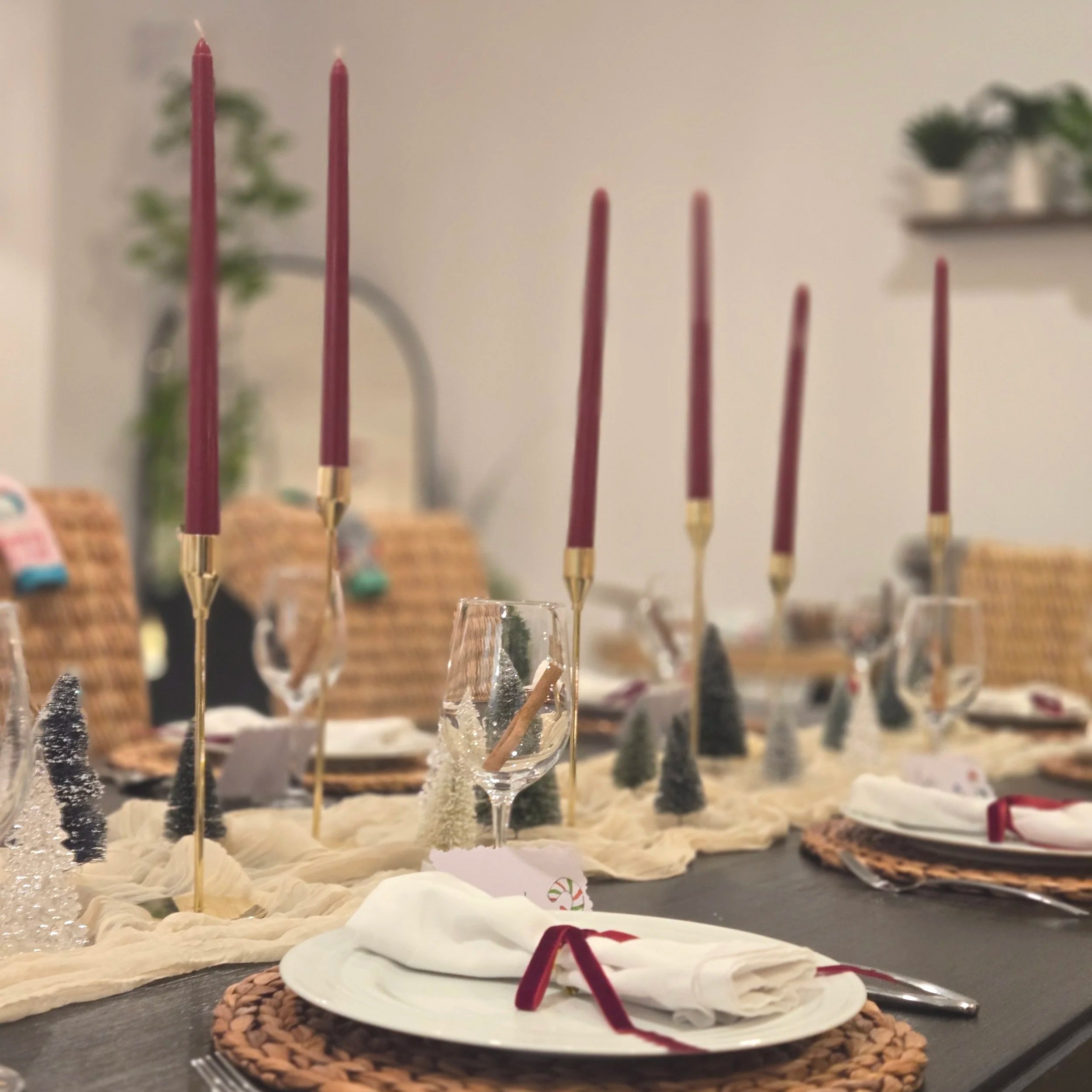 Christmas-themed table setting with gold candlesticks, burgundy candles, white napkins, and small decorative Christmas trees.