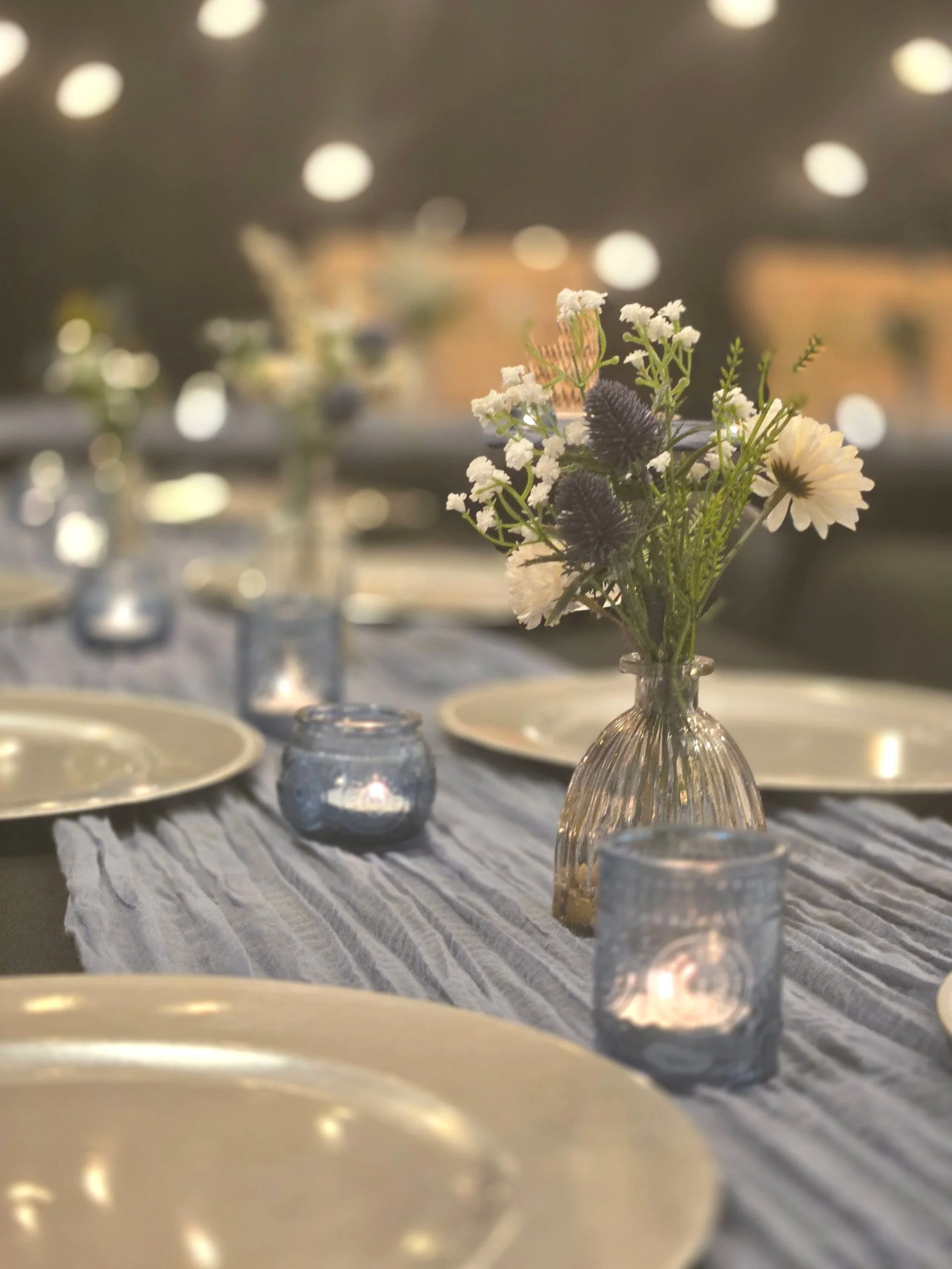 Table setting with gold chargers, blue candle holders and budvases at Oasis Events Collective in Sarasota FL.  Cozy, intimate event venue for baby showers, bridal showers, birthday parties, end of life celebrations near Lakewood Ranch, Ellenton, Veni