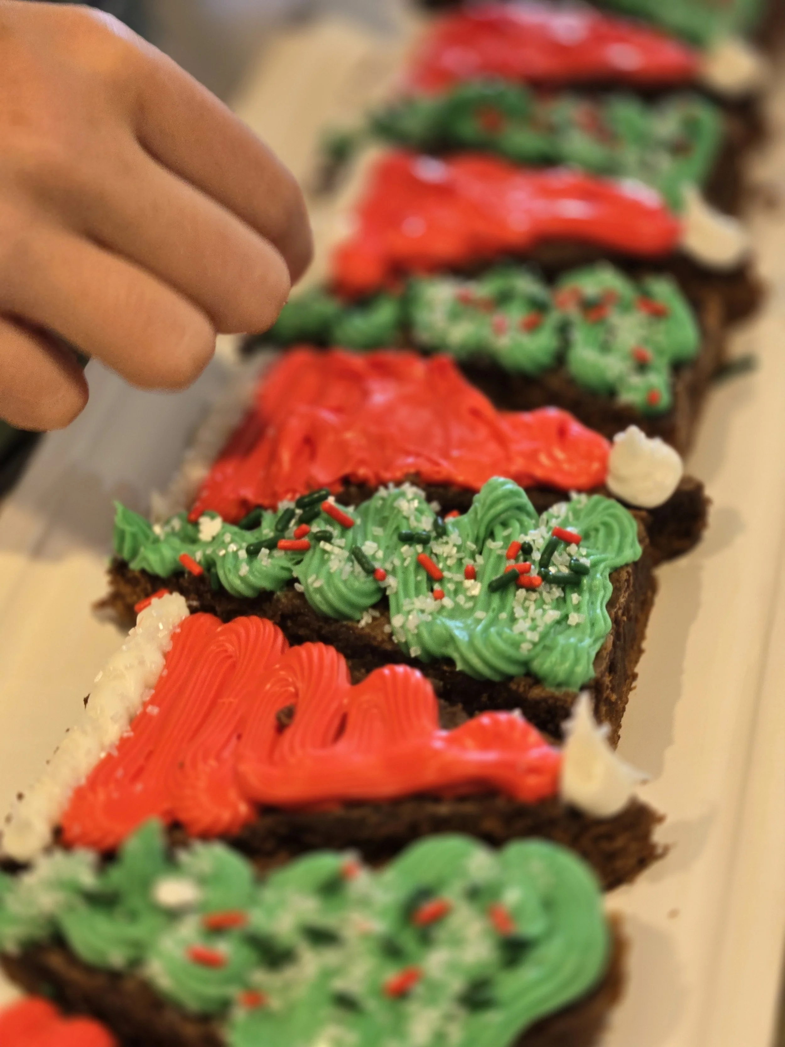 A row of Christmas-themed brownies decorated with red, green, and white frosting, sprinkles, and icing in holiday patterns.