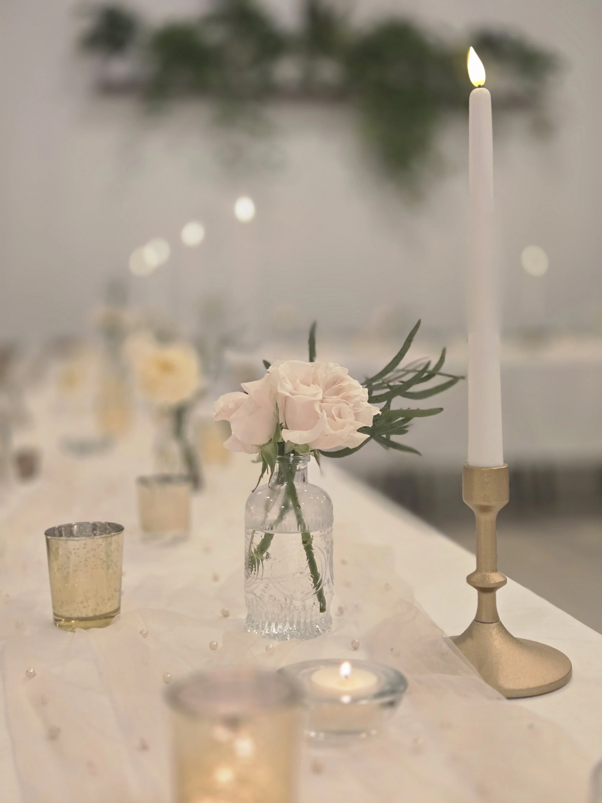 Budvases, gold candlesticks, gold votives and beaded table runners on table setting at a rehearsal dinner in the Oasis Events Collective venue in Sarasota FL