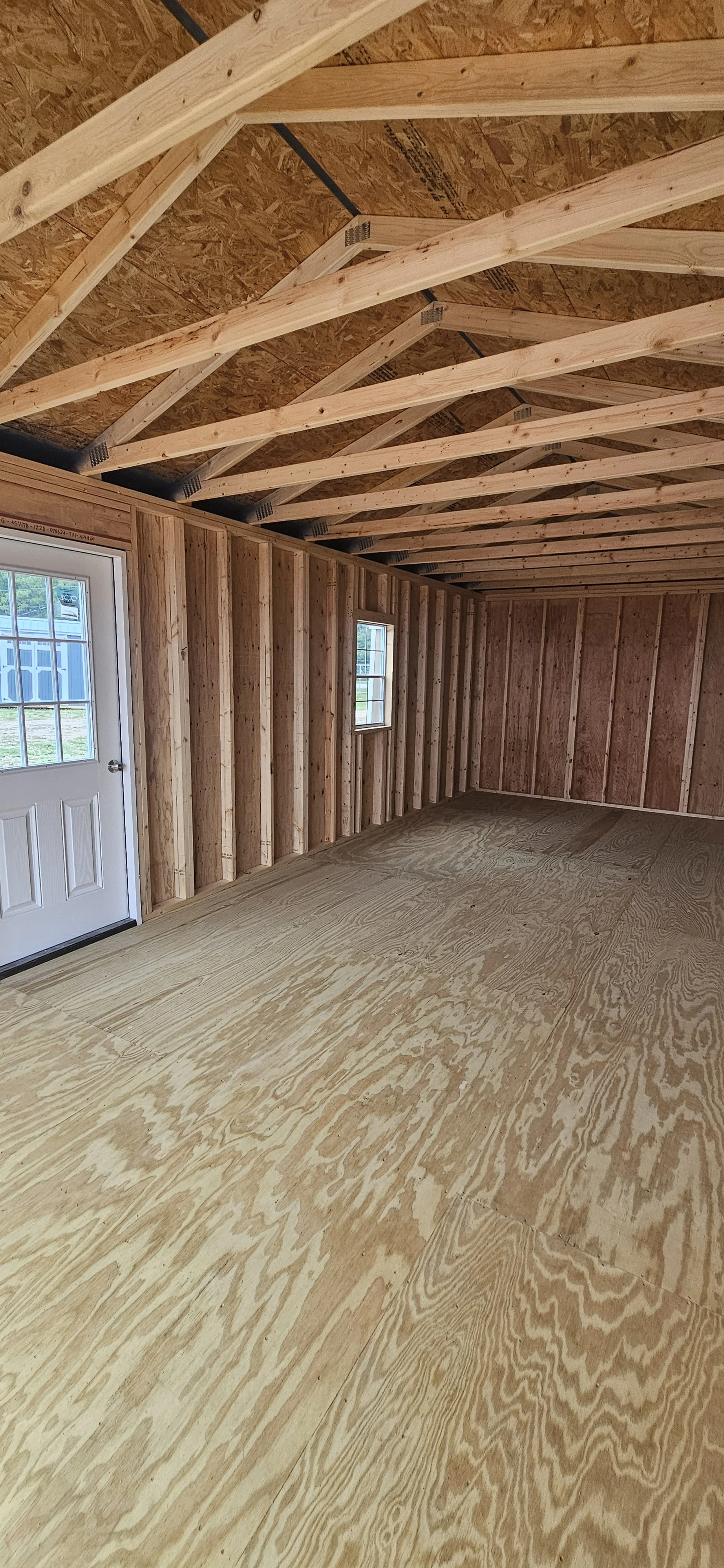 Interior of a new unfinished room with exposed wooden framing, plywood walls, and ceiling, with two windows and a door.
