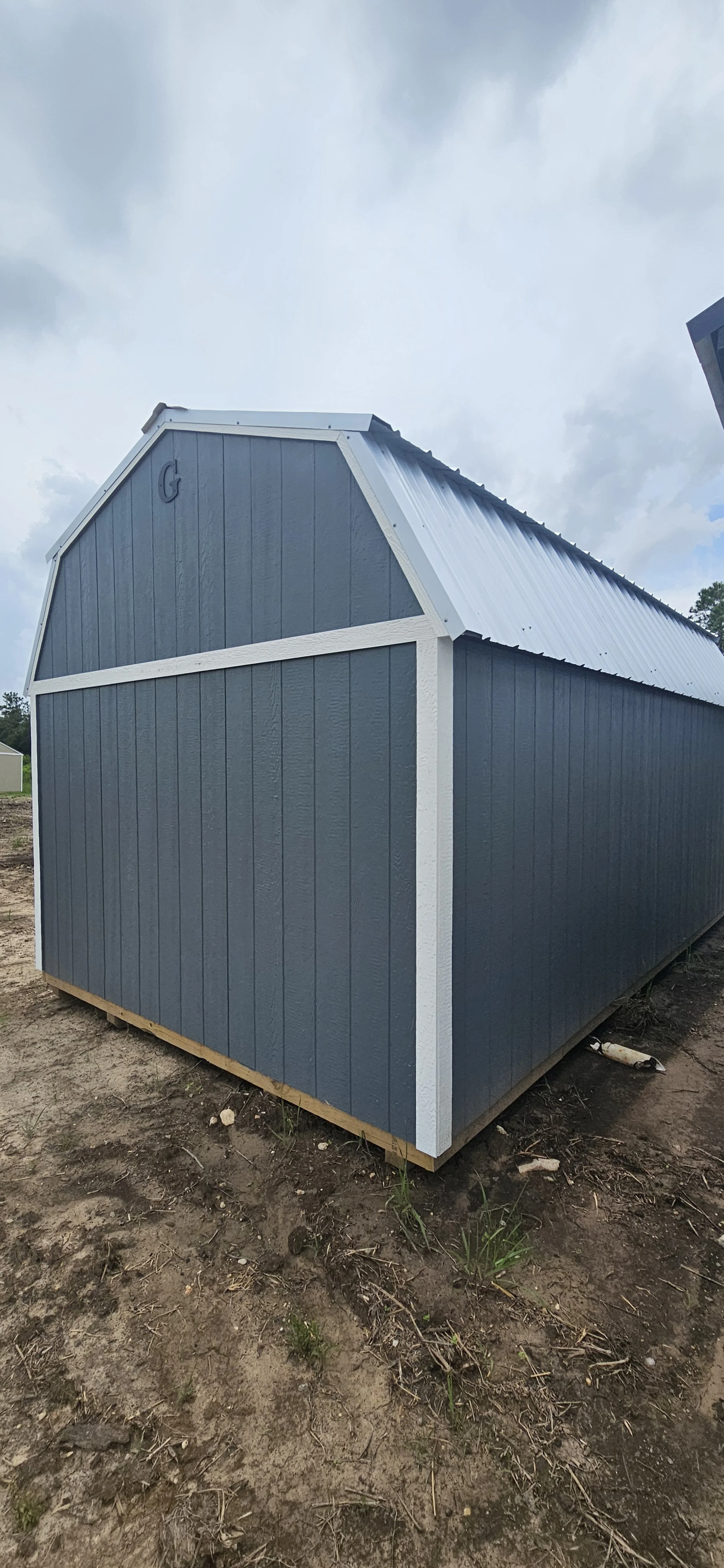 Blue and white shed with a gable roof on a dirt lot under cloudy sky.
