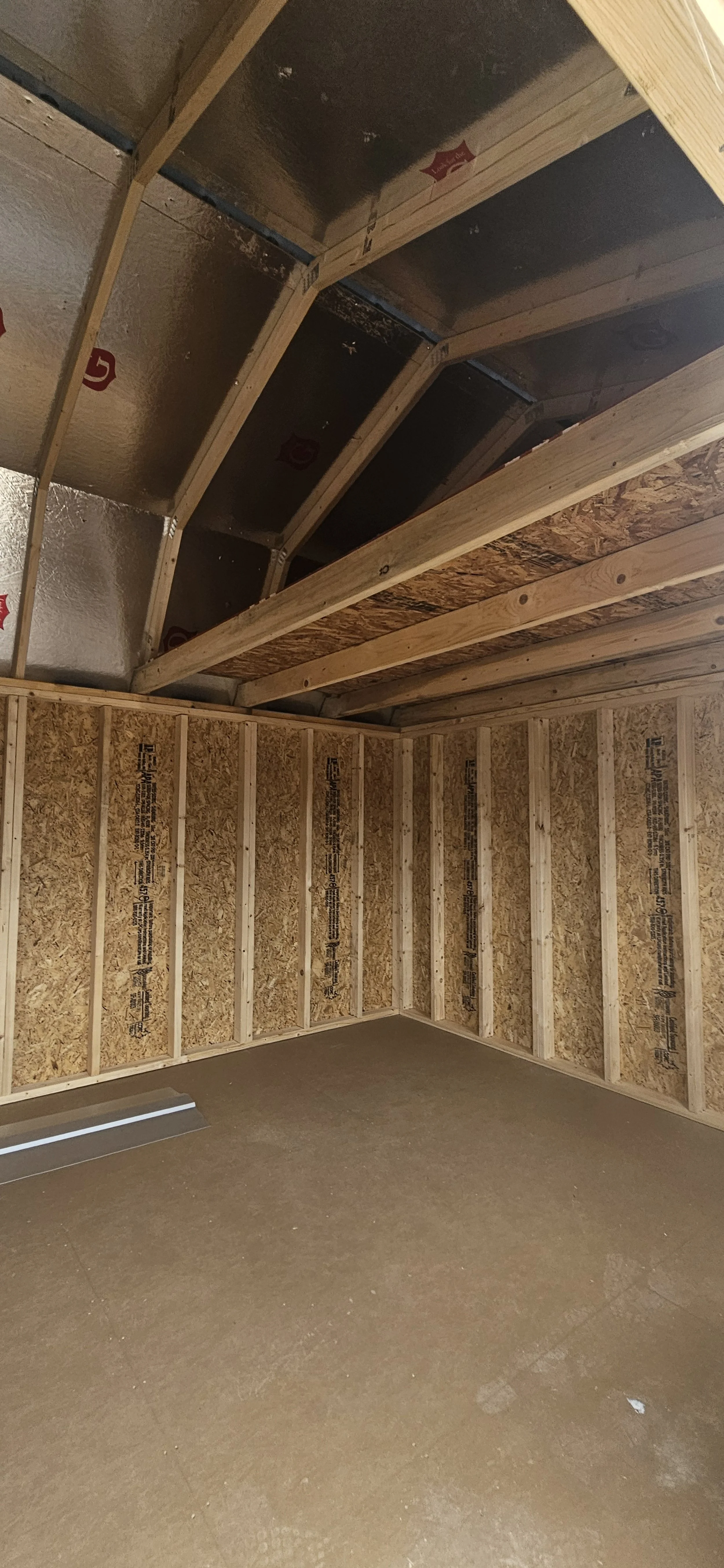 Unfinished room or closet with exposed wooden framing and sheathing, and a bare concrete floor.