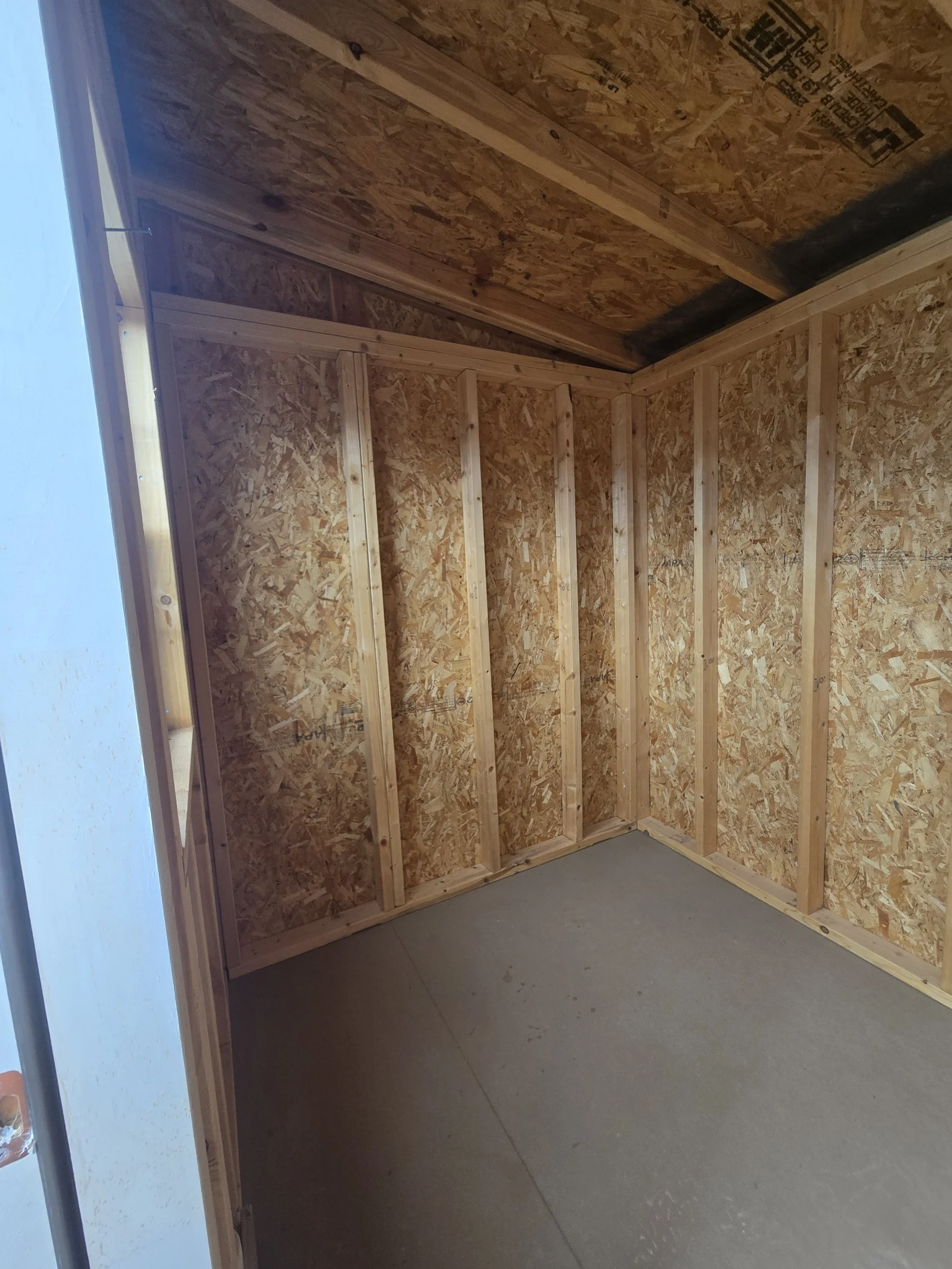 An unfinished room with plywood walls and a concrete floor, possibly a shed or small storage space under construction.