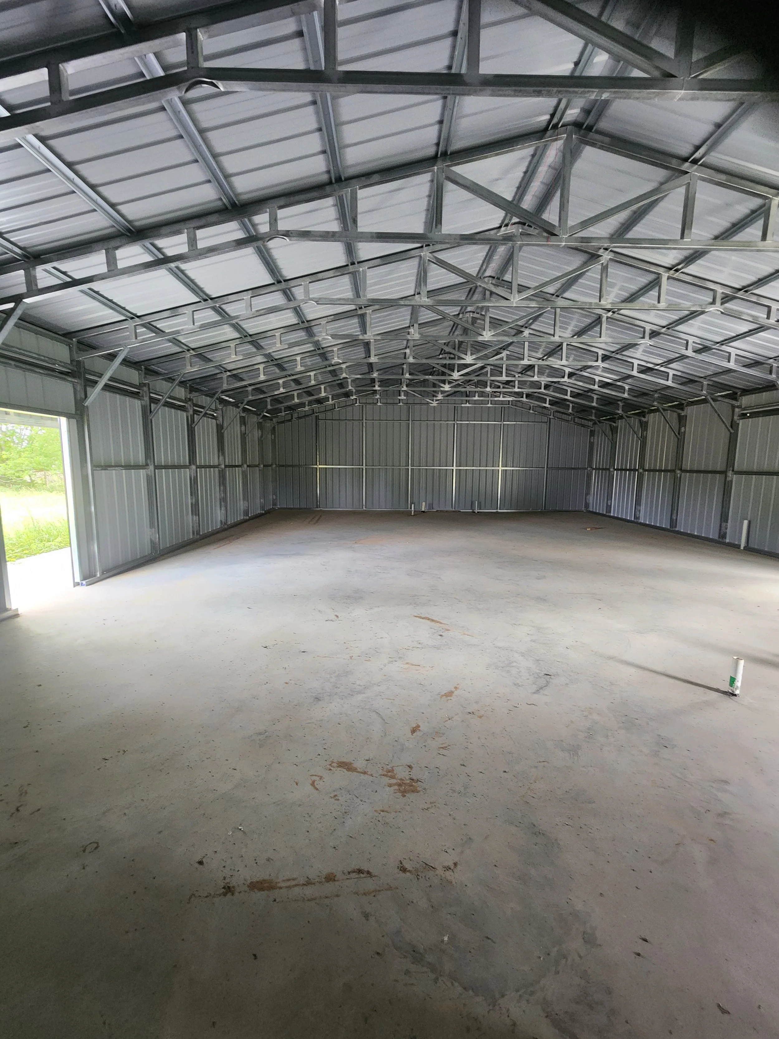 Empty metal building with concrete floor, metal walls, and a high ceiling under construction.
