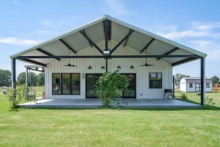 A modern white house with a large covered patio area, ceiling fans, and surrounding green lawn under a blue sky.