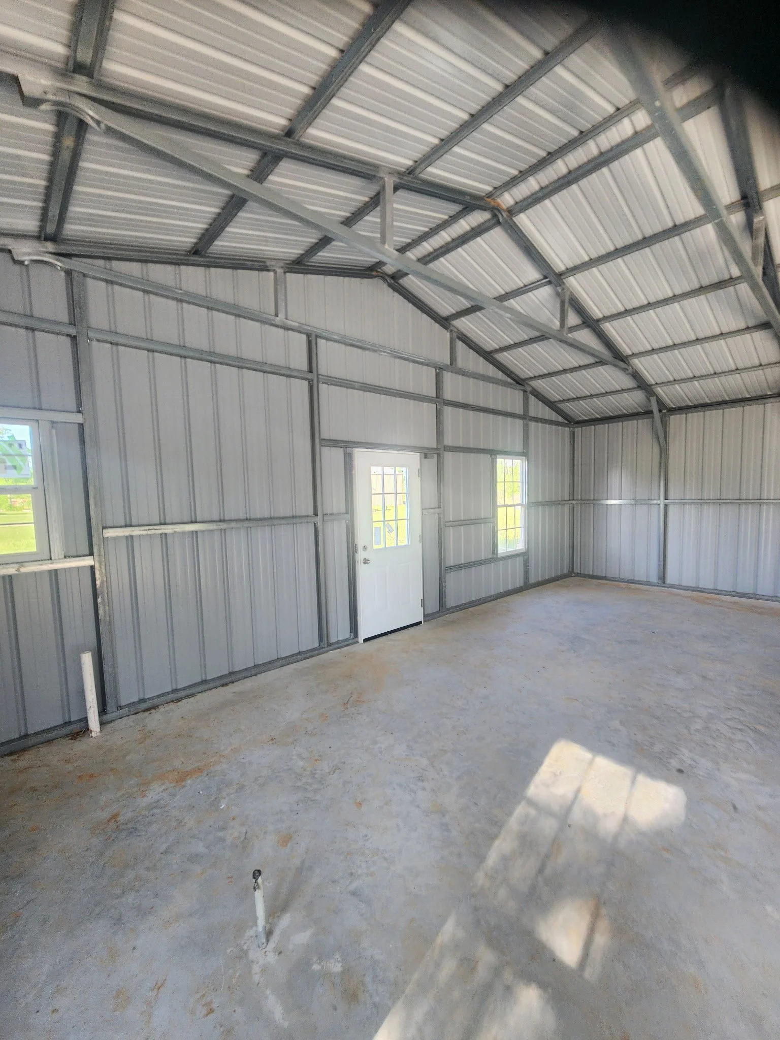 Interior of an unfinished metal building with concrete floor and windows, featuring a door and metal framing.