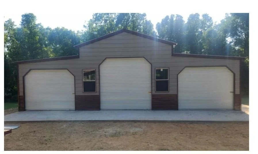A large garage with three roll-up doors and two small windows, set against a backdrop of trees.
