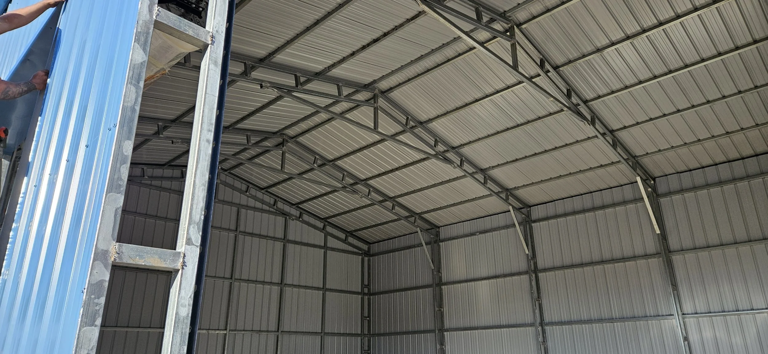 Image of the interior of a metal building under construction, showing the curved metal roof and walls, with a metal scaffolding structure on the left side.