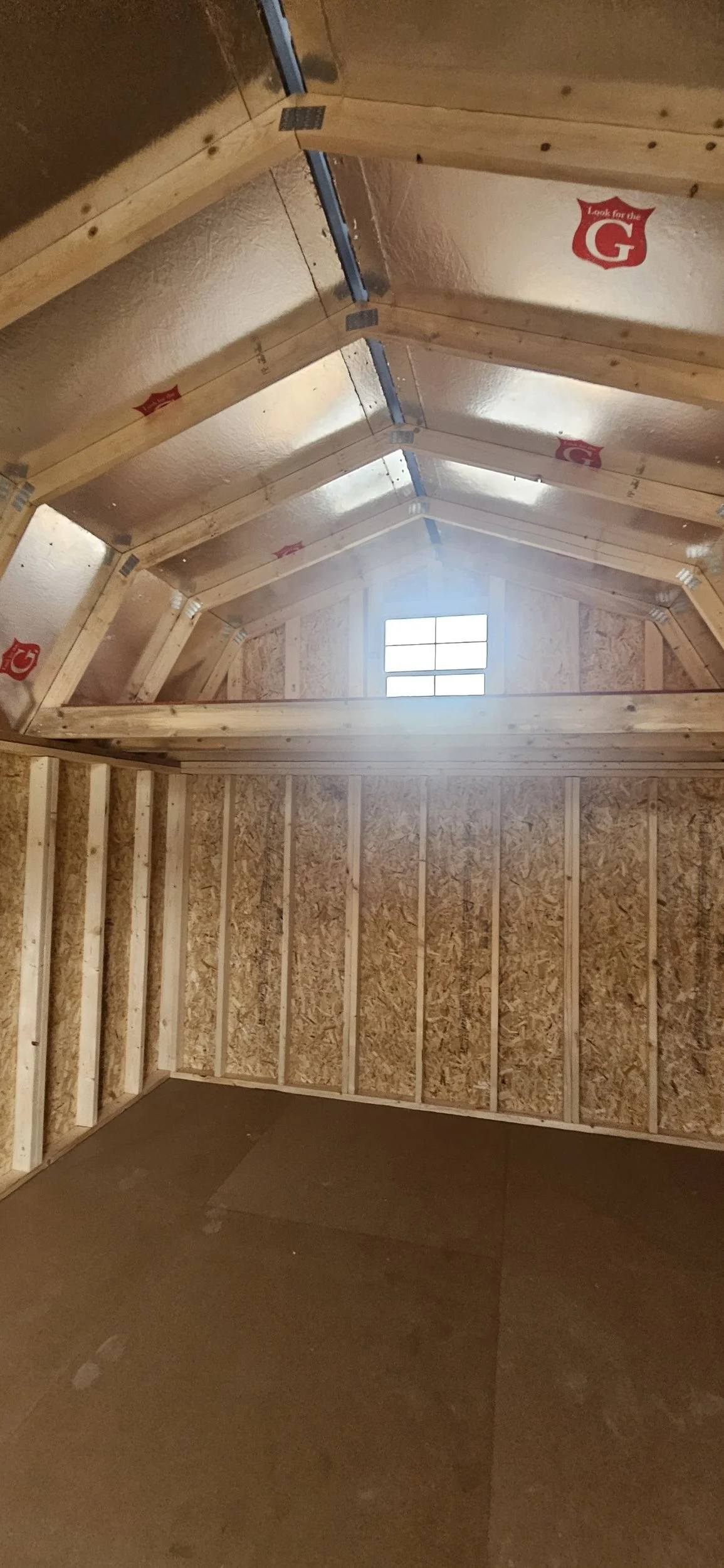 Photo of an attic under construction showing wooden framing, insulation panels, and a small window at the end.