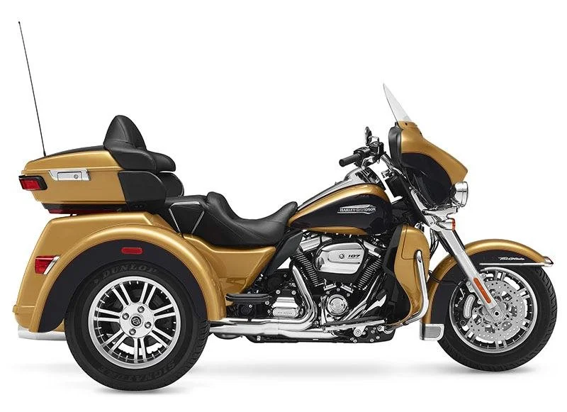 Gold Harley-Davidson touring trike motorcycle with windshield, saddlebags, passenger backrest, and two rear wheels