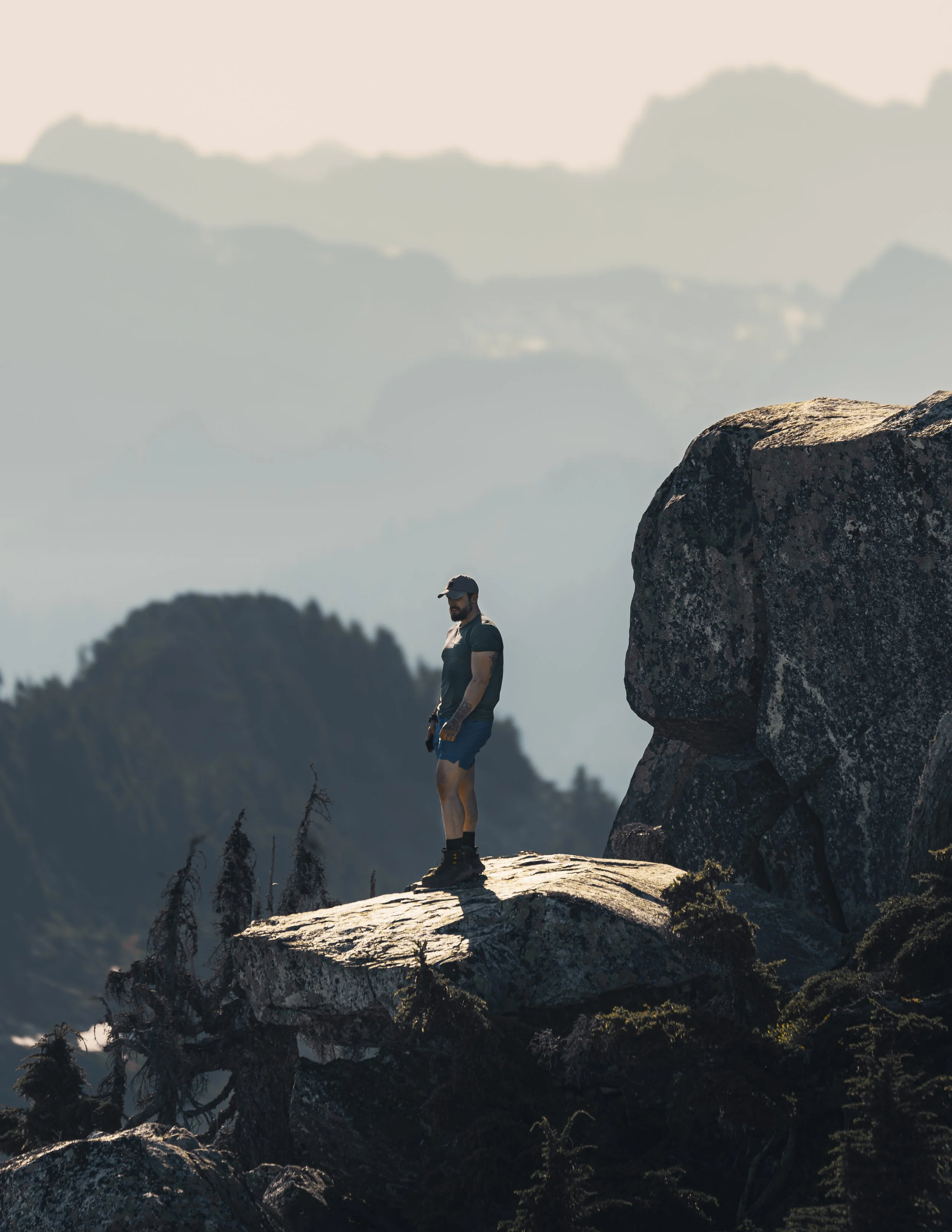 Hiker standing on a dramatic granite ledge looking out at hazy mountain layers at Mount Pilchuck.
A true sense of scale and perspective. A hiker stands on a dramatic granite precipice looking out over the hazy, endless layers of the Washington wilder
