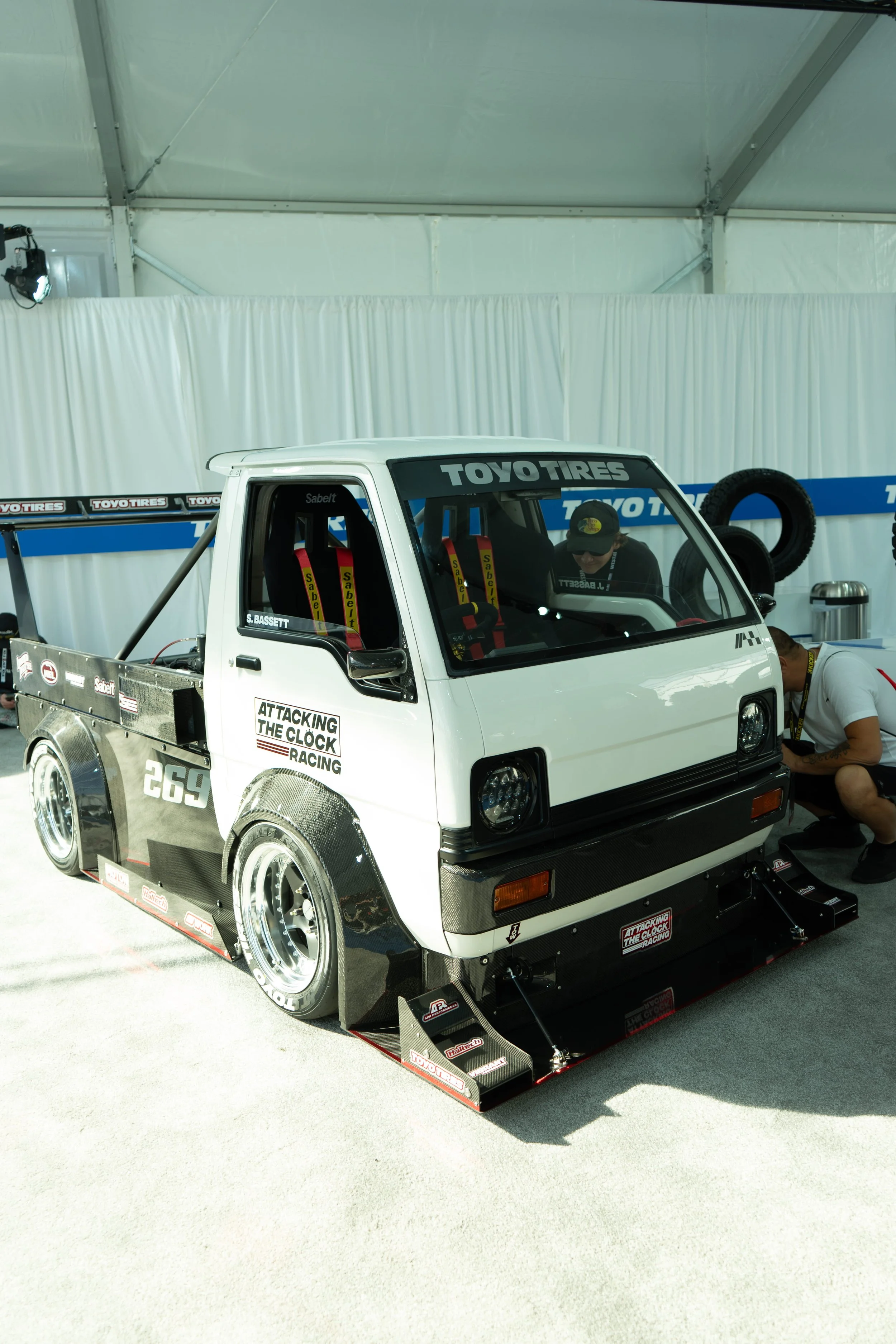 Full front angle of a custom white Time Attack Kei truck with a carbon fiber aero kit and Sabelt racing seats at SEMA Las Vegas.
Full view of the wild Attacking the Clock Racing Kei truck at SEMA. Featuring extreme carbon fiber aero, Toyo Tires, and 