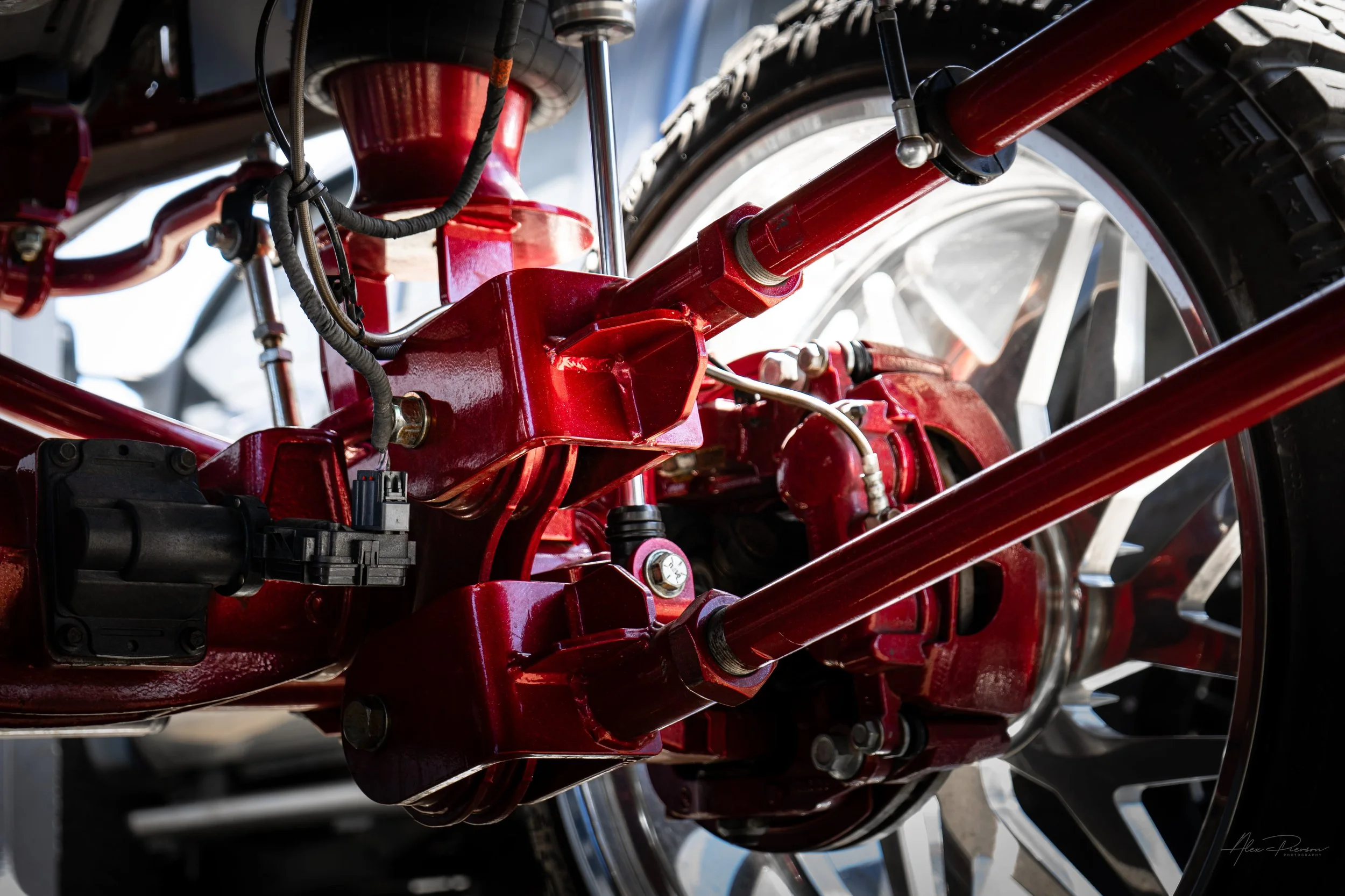 Detailed undercarriage shot of a custom Ram 2500 highlighting the heavy-duty red powder-coated trailing arms, sway bar links, and Kelderman air ride components.
 Red trailing arms, Kelderman suspension parts, truck sway bar, Ram 2500 lift kit.
heavy-